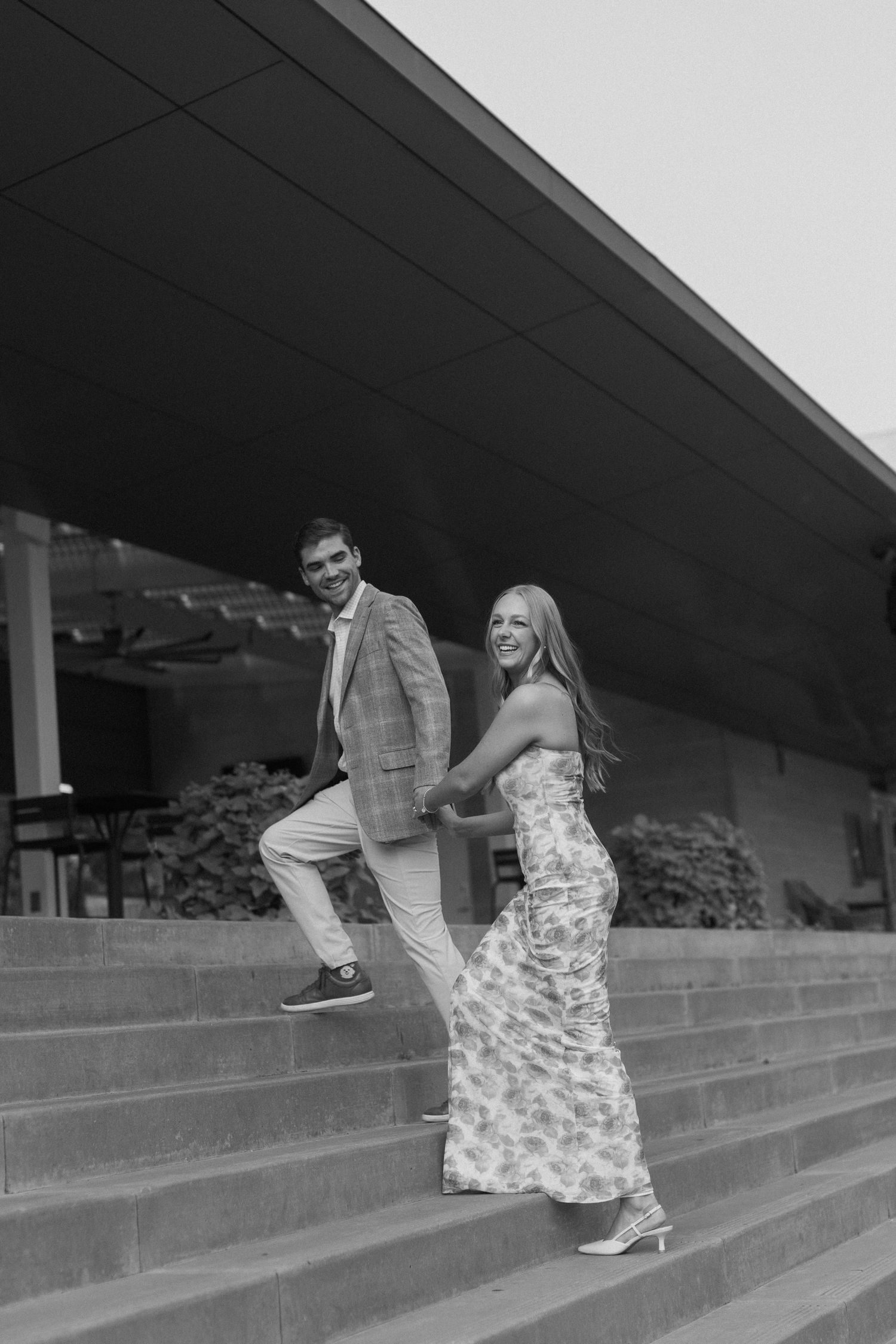 A sequence of black and white photos shows a couple playfully running up concrete steps together while laughing.