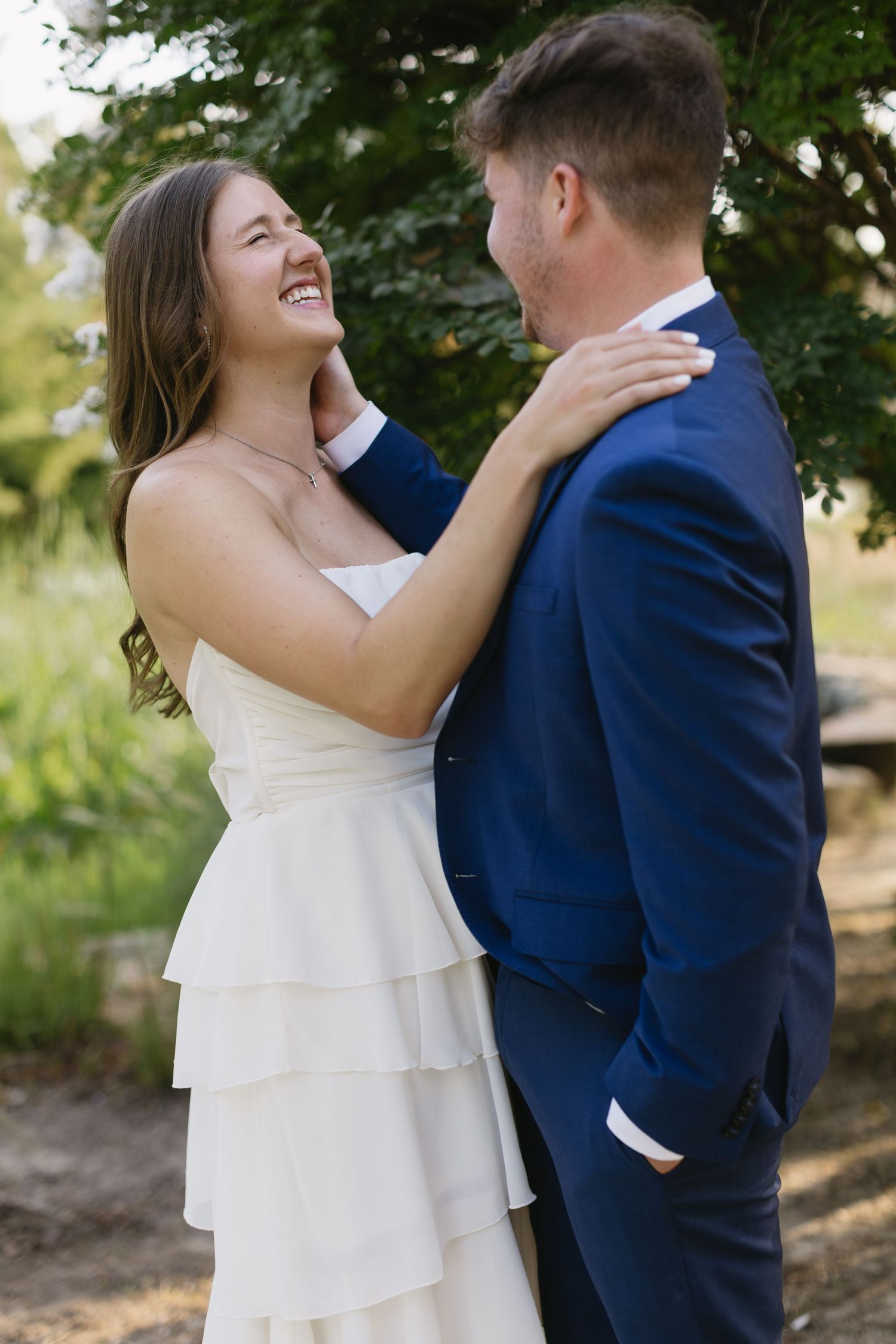 A romantic wedding moment with the couple embracing in a sun-dappled outdoor garden setting.