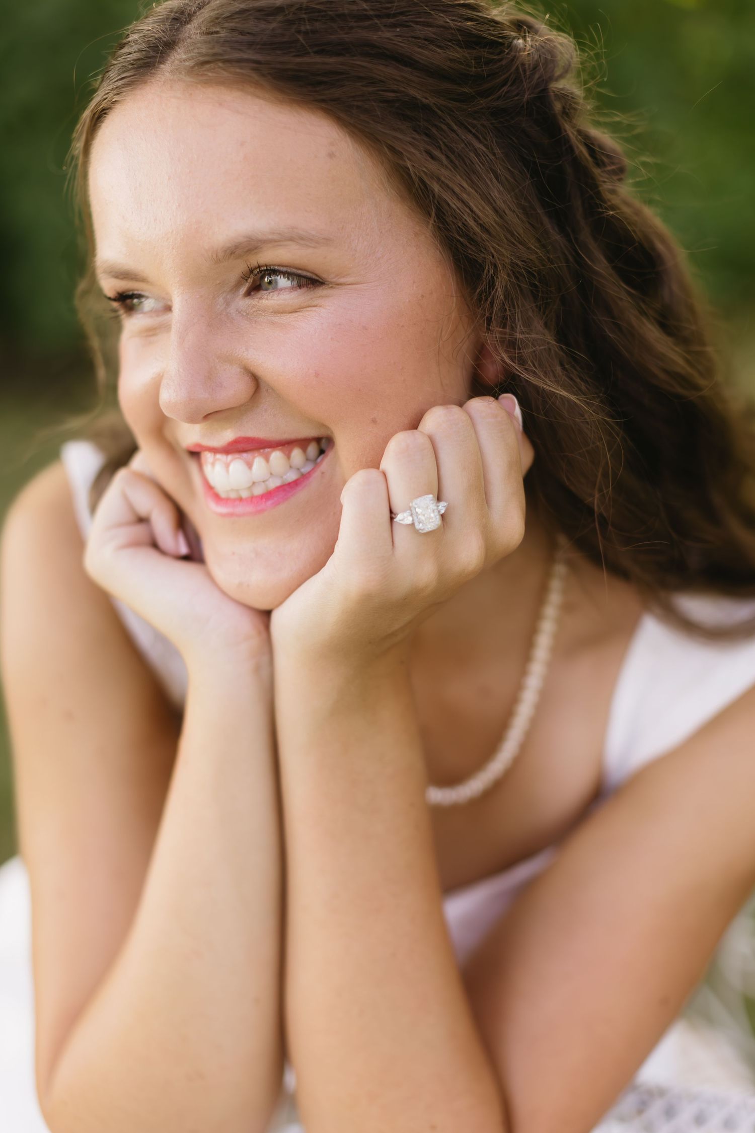 Close-up portrait showing pearl necklace and joyful expression against a natural outdoor background.