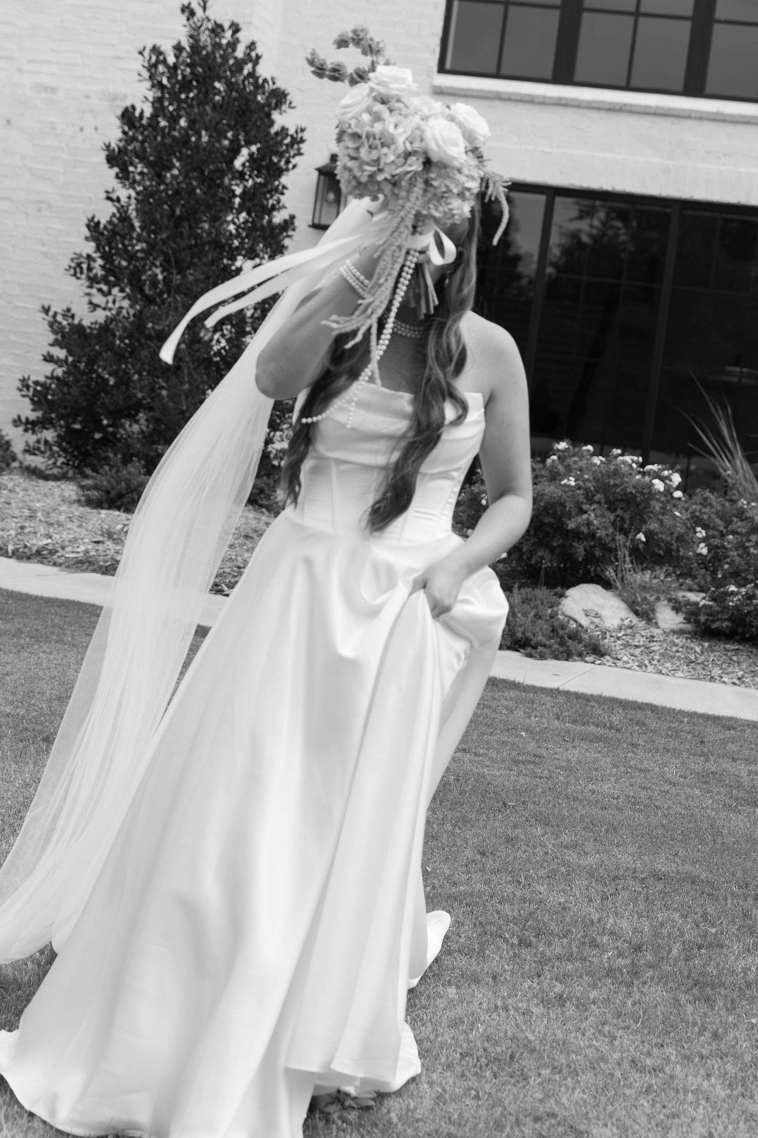 Elegant white wedding dress with flowing veil captured in black and white outdoors.