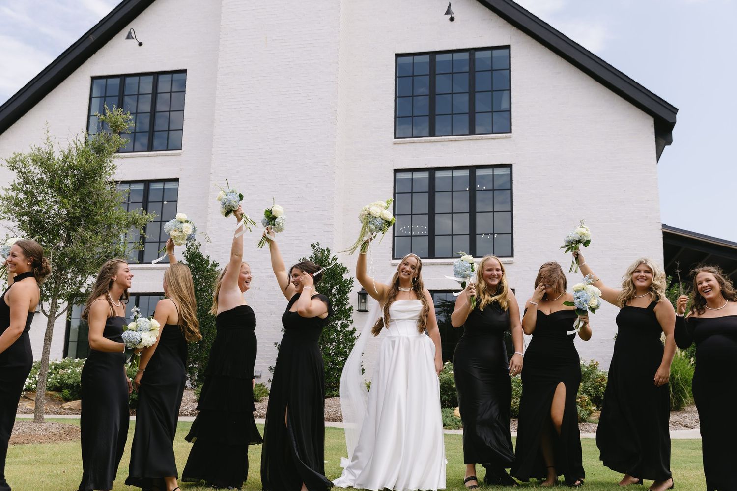 Wedding party in black attire lined up outside white building with black windows.
