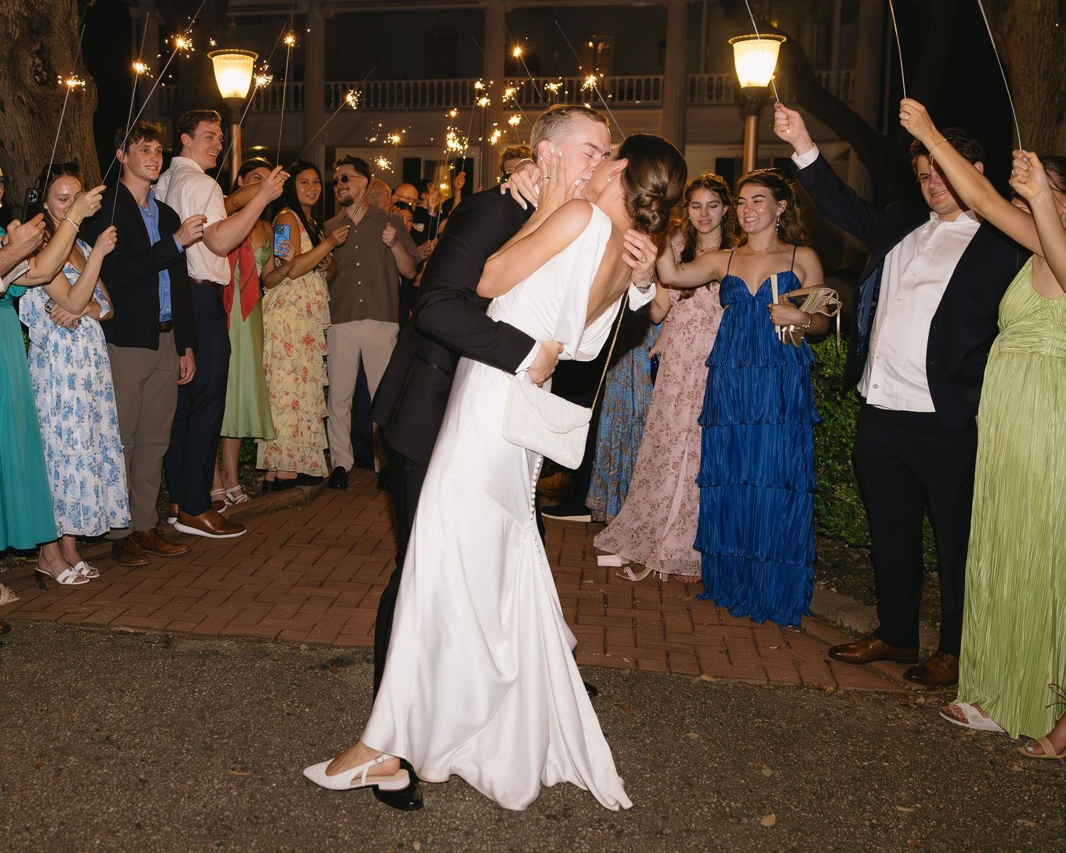 Wedding reception guests forming a tunnel of sparklers at night as newlyweds dance through.