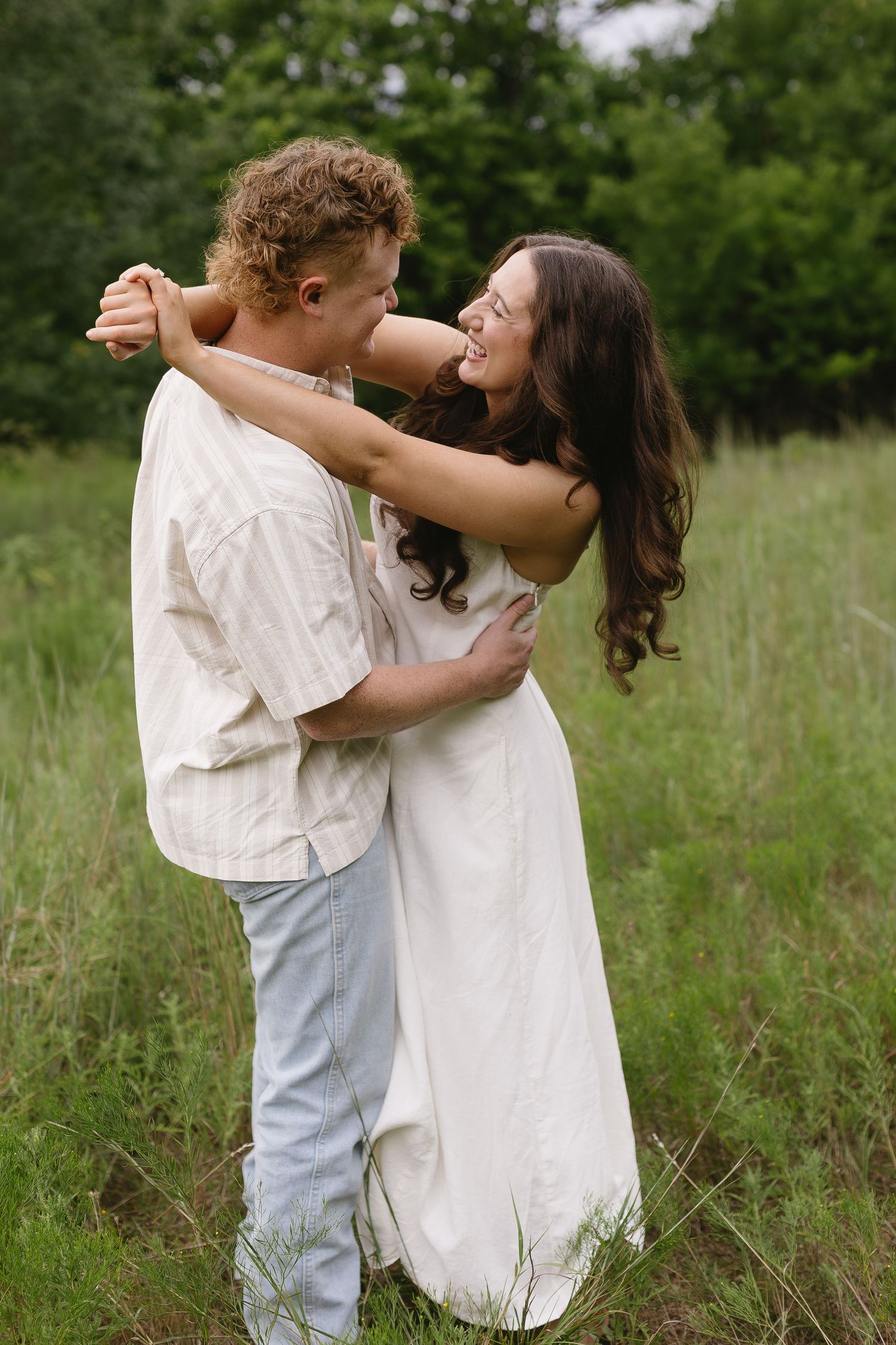 Two people in white and denim share playful moments together in a sunny meadow.