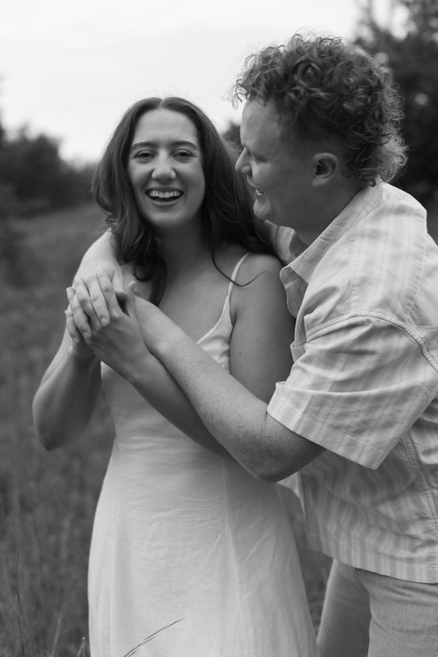 A romantic black and white photo series showing a couple embracing and laughing in a natural outdoor setting.