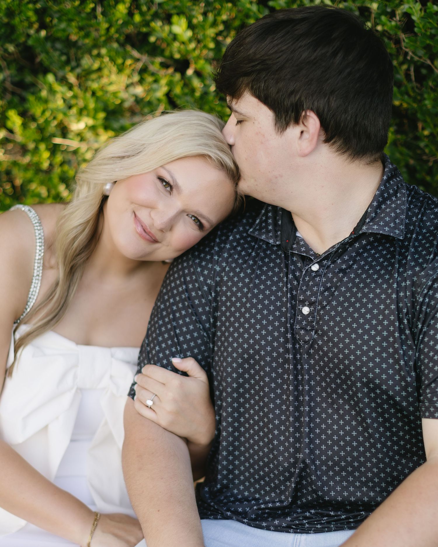 A romantic couple sits close together in a garden setting wearing white and navy polka dot outfits.