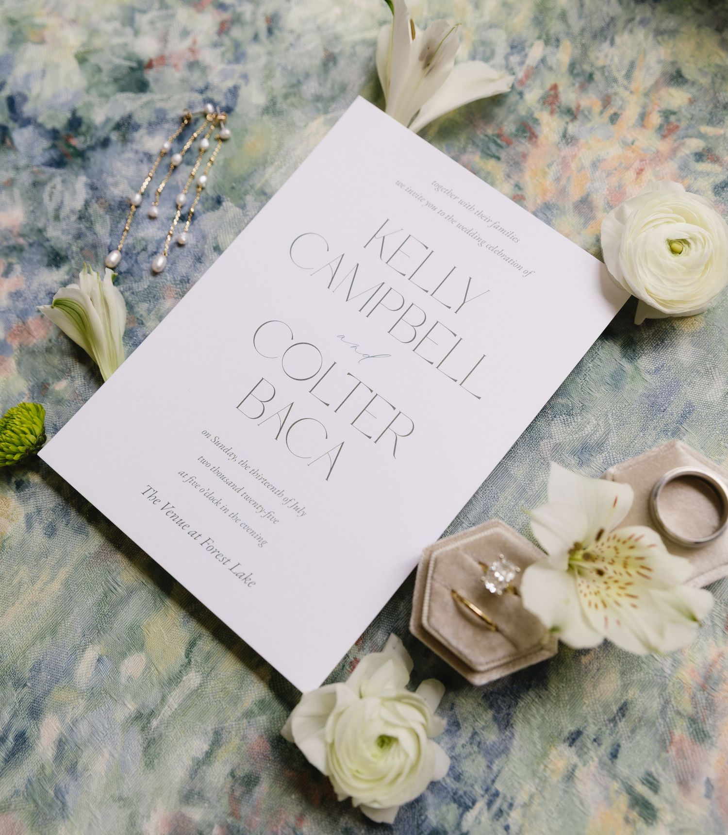 Elegant white wedding invitation with white flowers and hexagonal ring boxes on marbled surface.