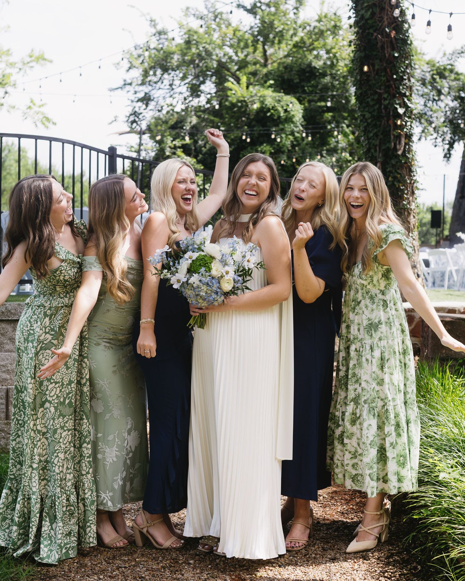 Wedding party in floral dresses and navy blue gowns posing together in garden setting.