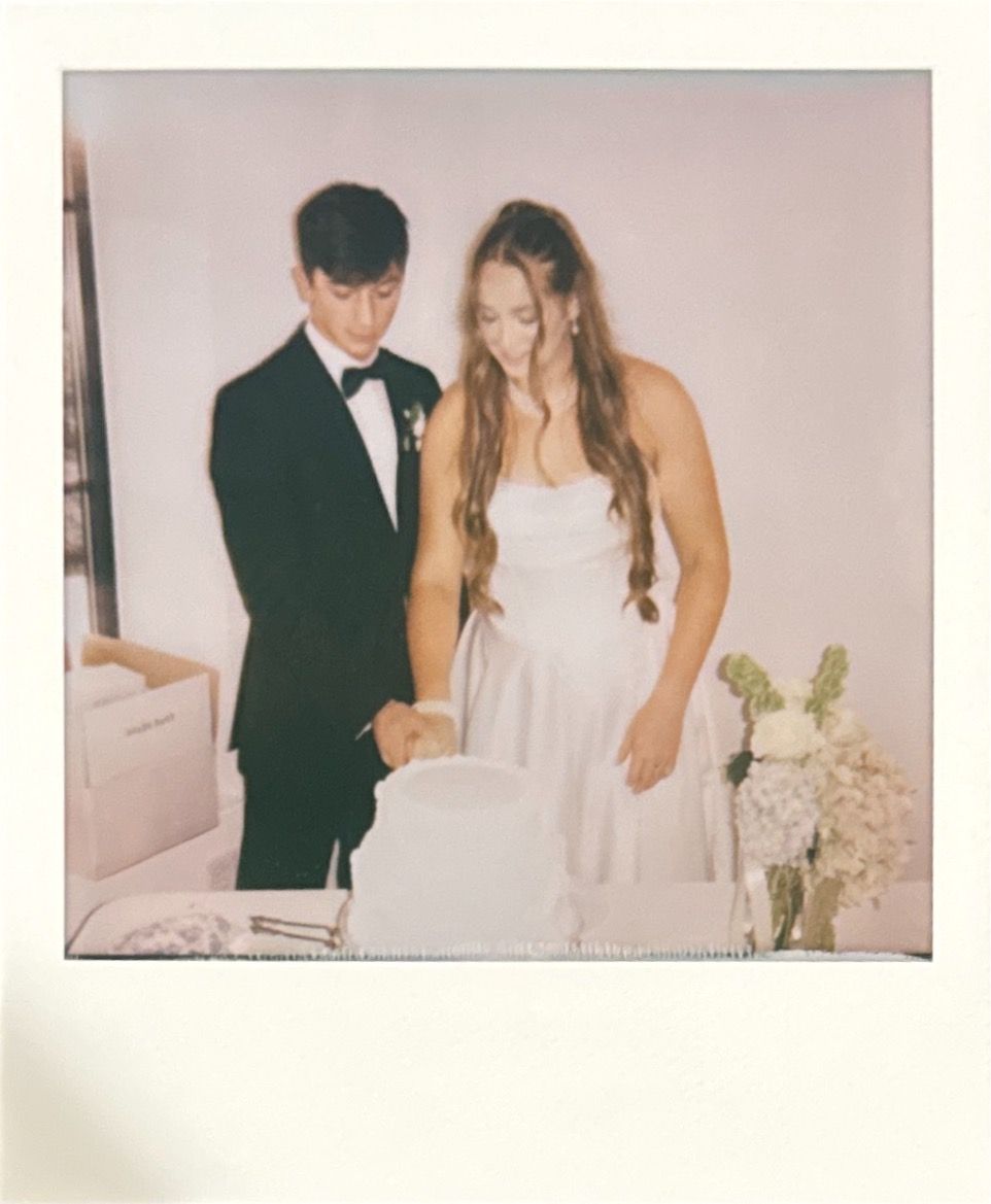 A couple shares a moment together at what appears to be a wedding reception, with white floral decorations in the background.