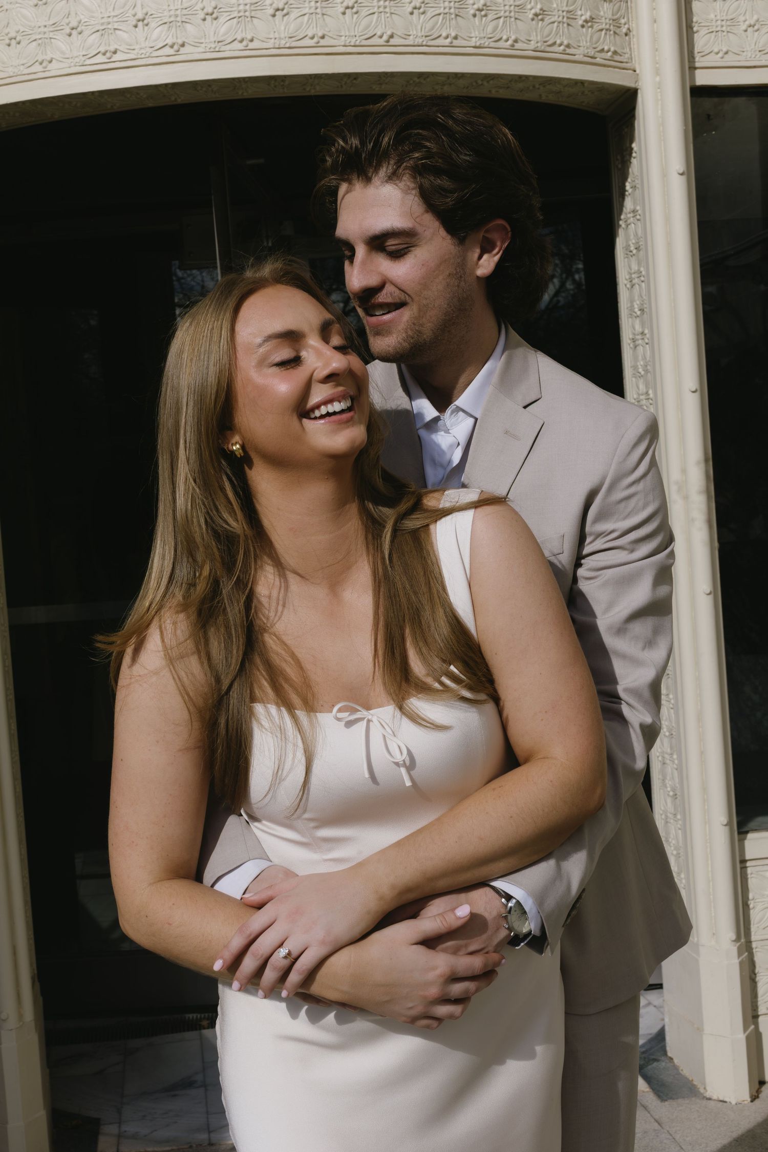 Intimate moments captured between couple in white dress and beige suit by architectural details.