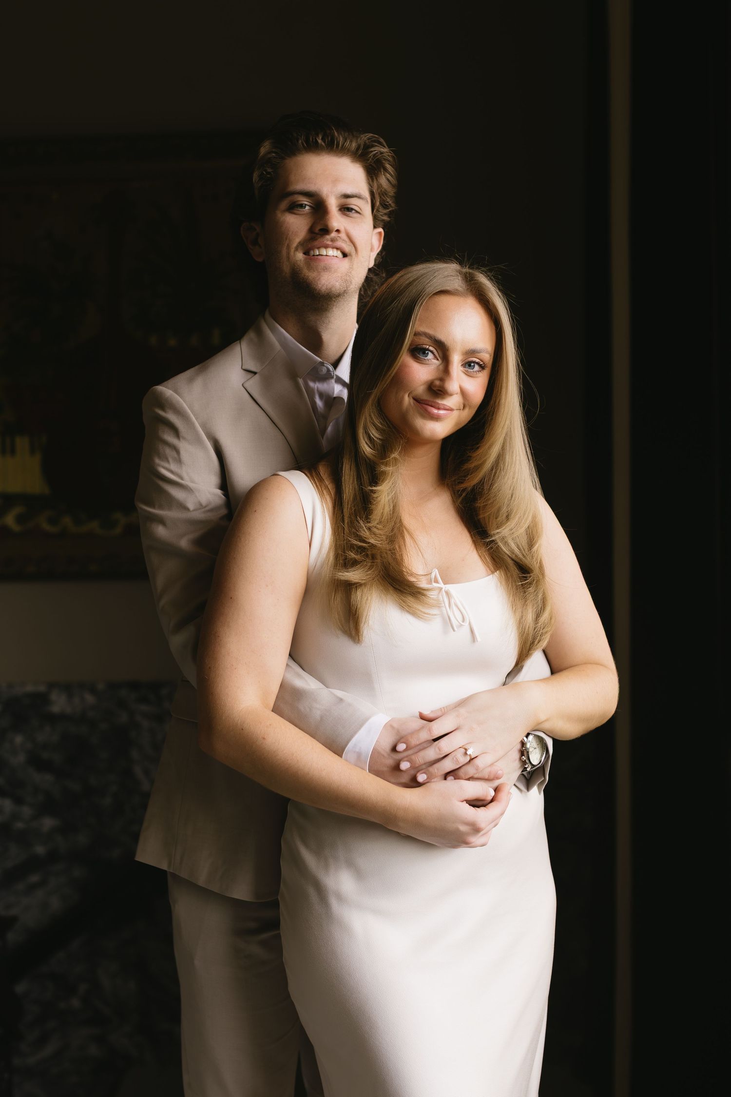 An elegant couple poses together in formal attire against a dark background.