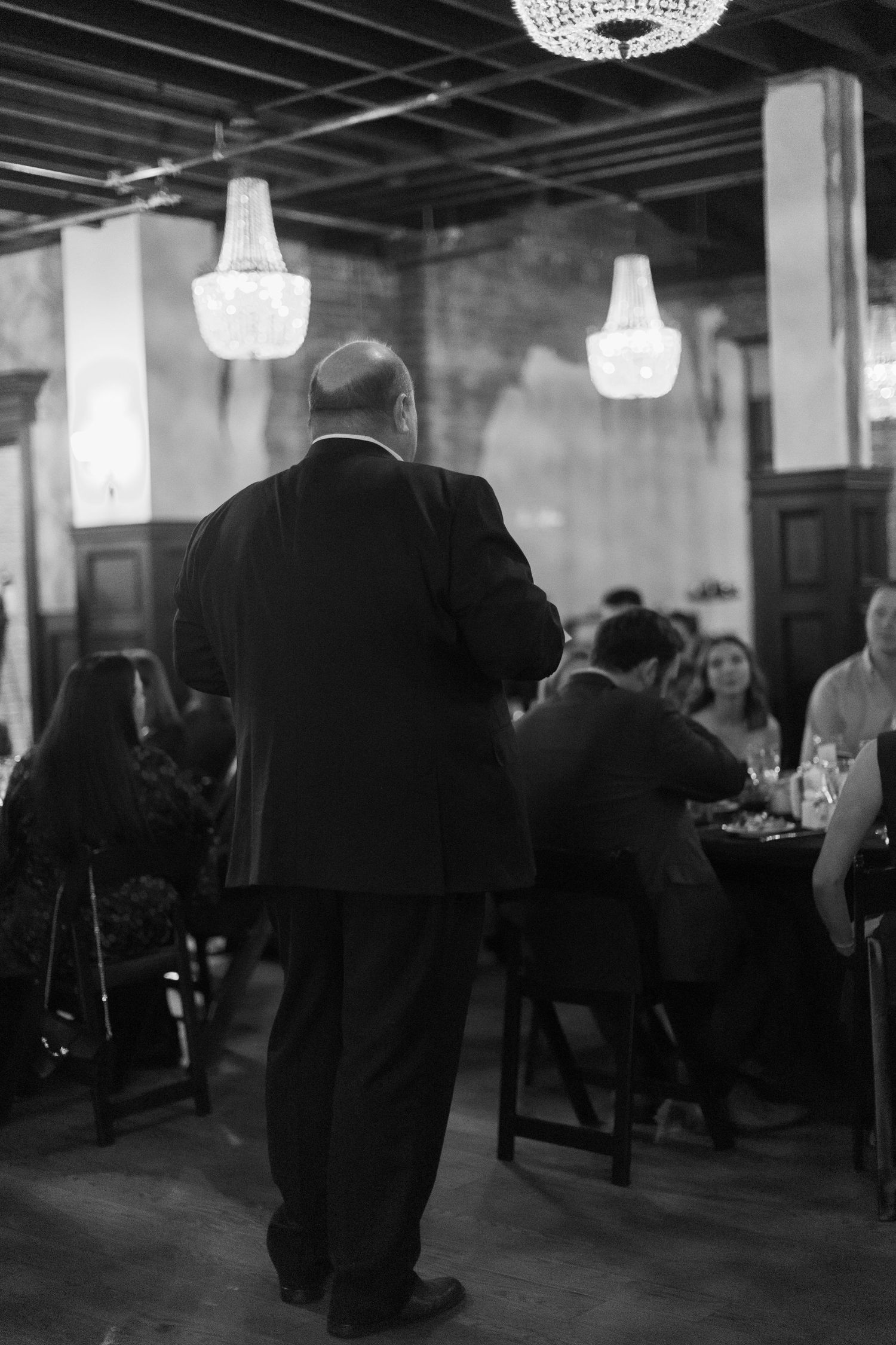 Dimly lit event space with crystal chandeliers and silhouettes of people mingling.