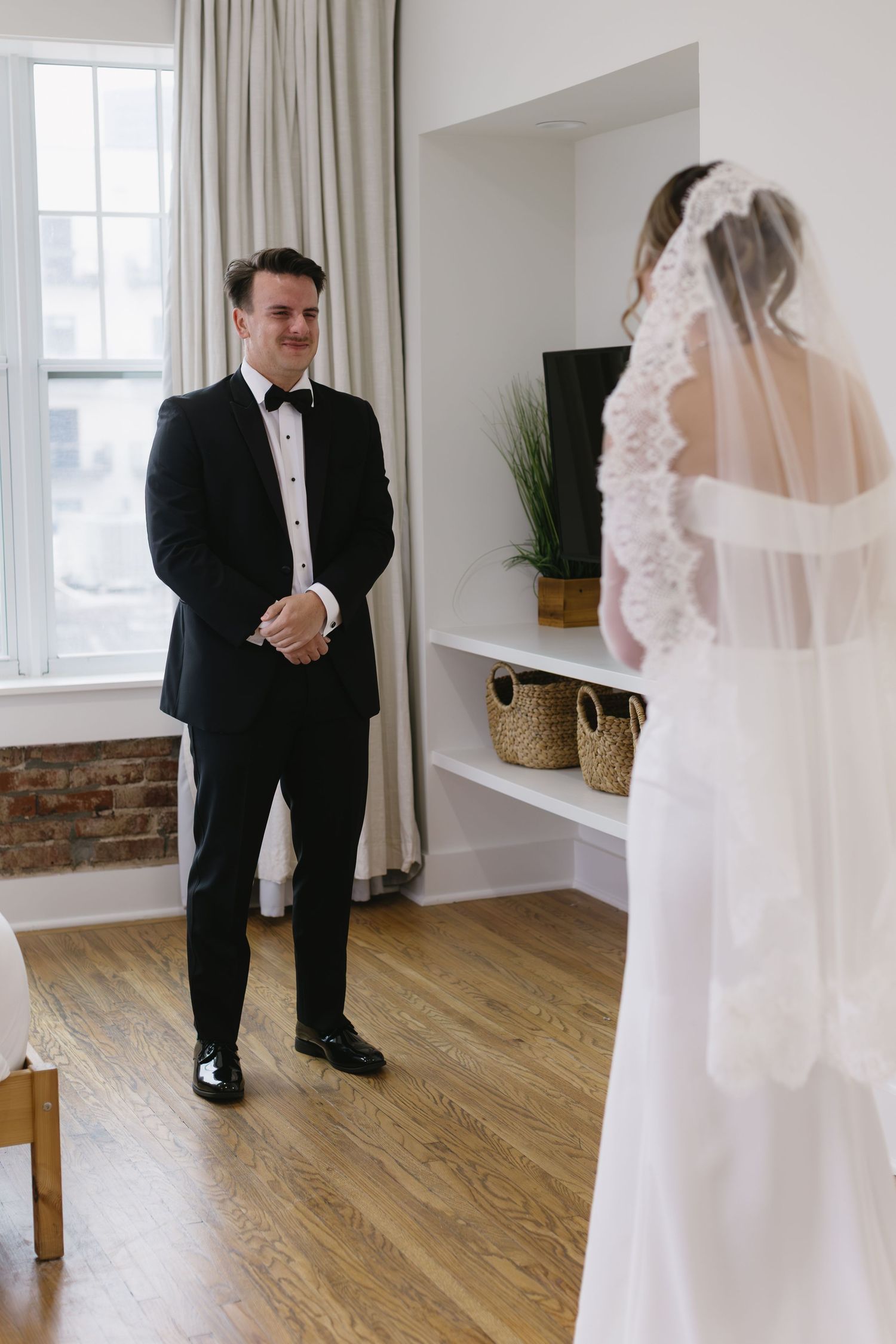 Emotional first look between bride and groom in a modern white room with wooden floors.