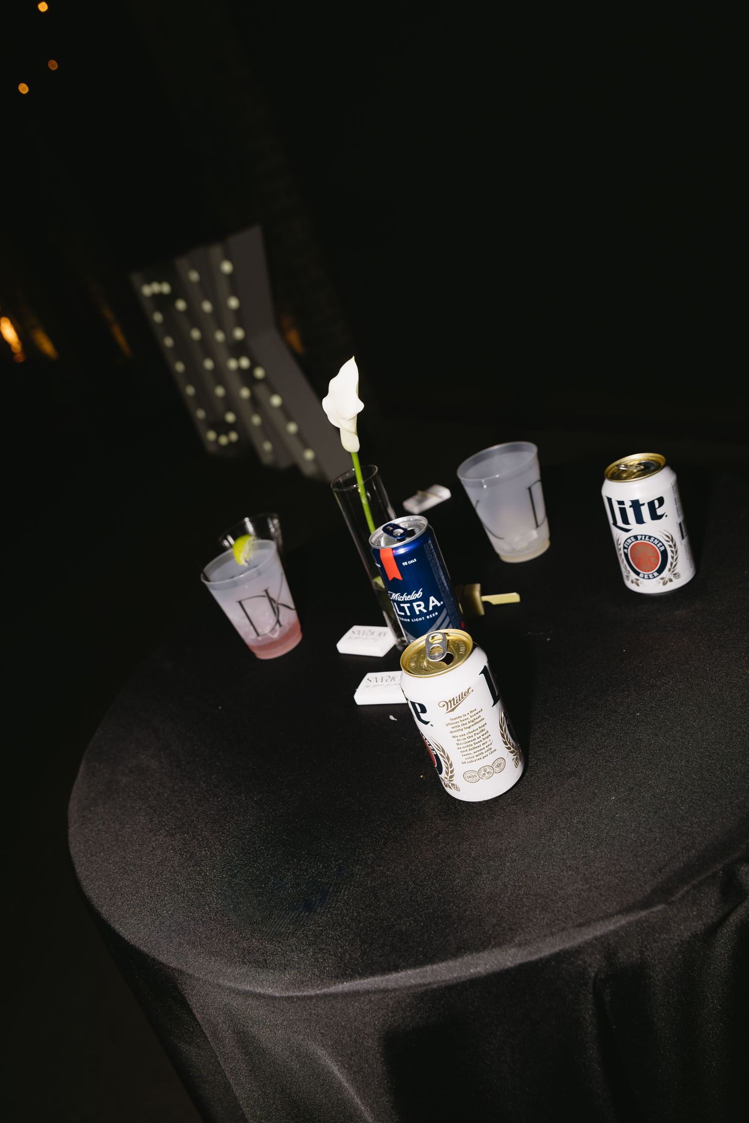 Dark table surface with scattered beer cans and cups illuminated by dim lighting.