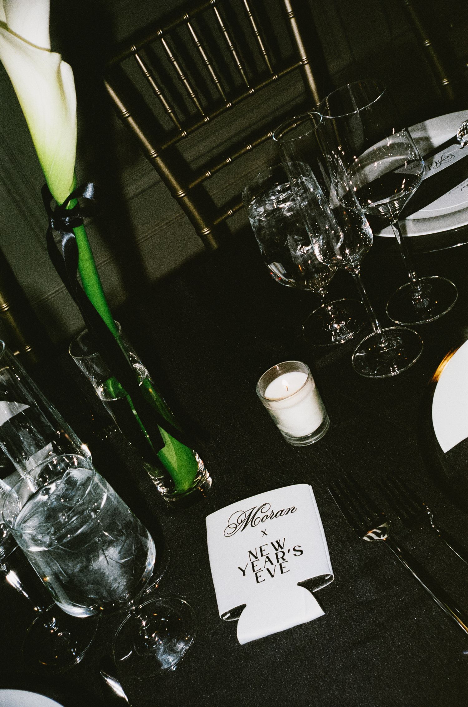 Wedding reception table settings with wine glasses and name cards in dark lighting.