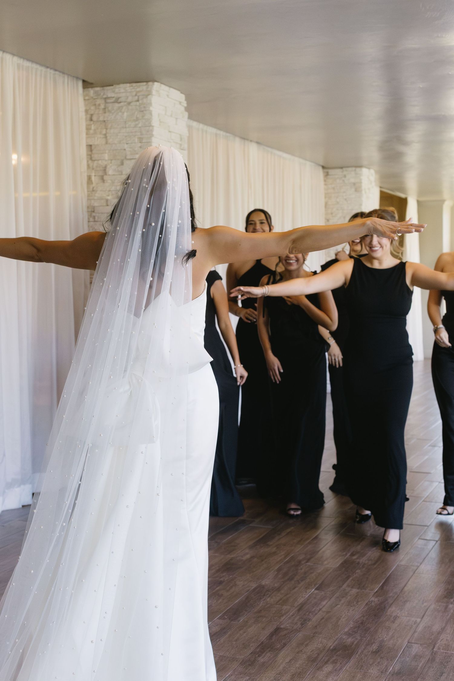Bridesmaids in black dresses line up for a fun group photo in an indoor venue.