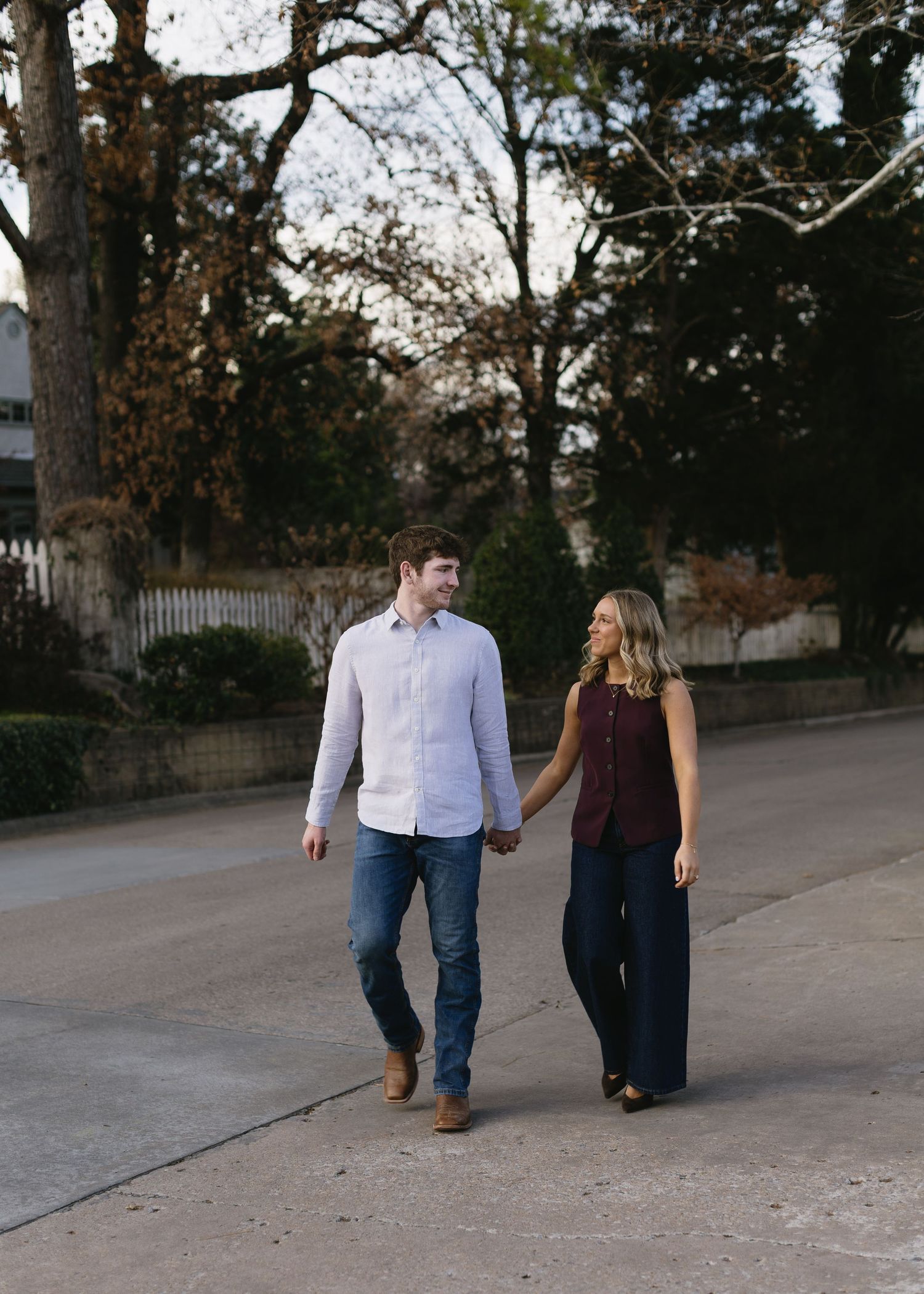 A couple walks hand in hand along a tree-lined path during autumn.
