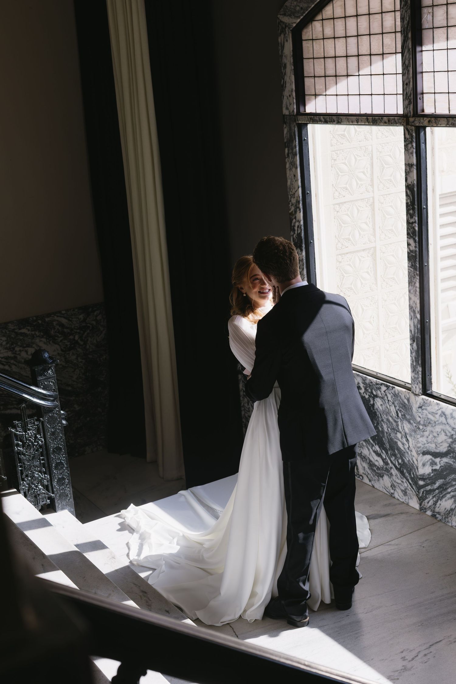 Wedding couple sharing a private moment by a window in dramatic lighting.