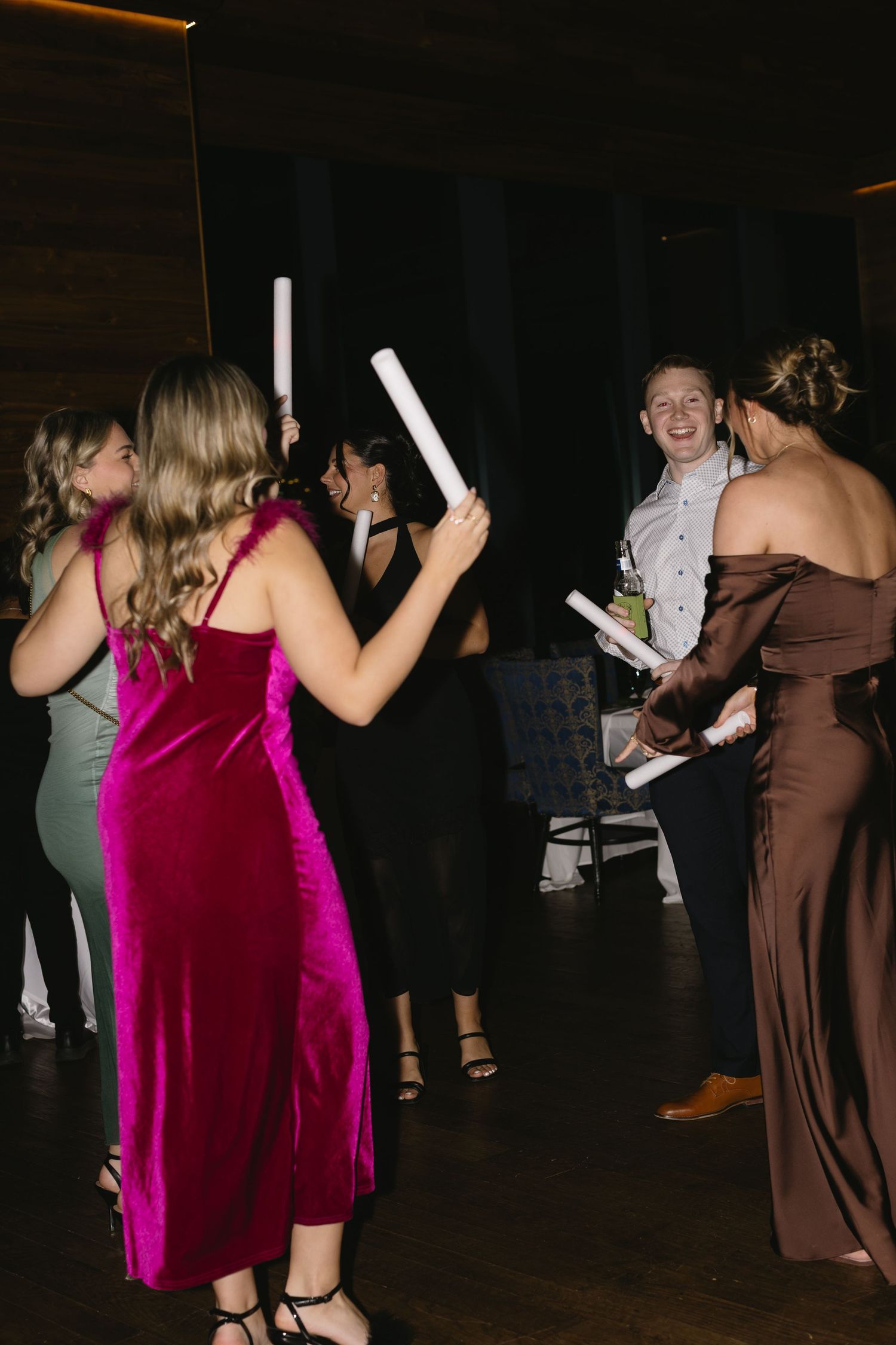 Wedding reception guests dancing and celebrating in a dark venue with glow sticks.