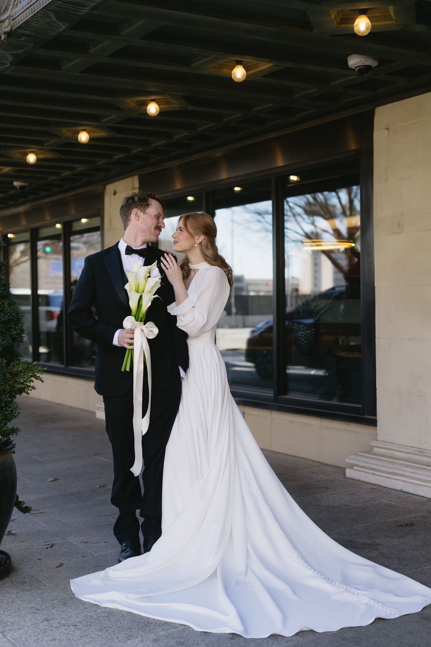 Wedding couple embracing outdoors with flowing white dress and classic tuxedo.