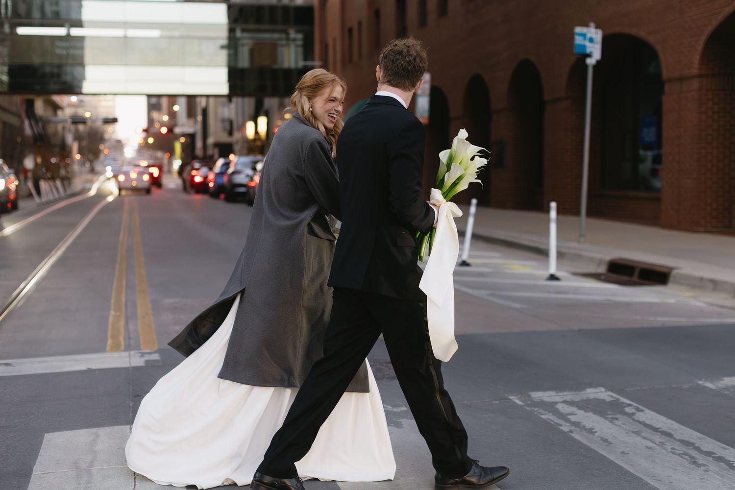 A wedding couple walking together on an urban street with brick buildings.