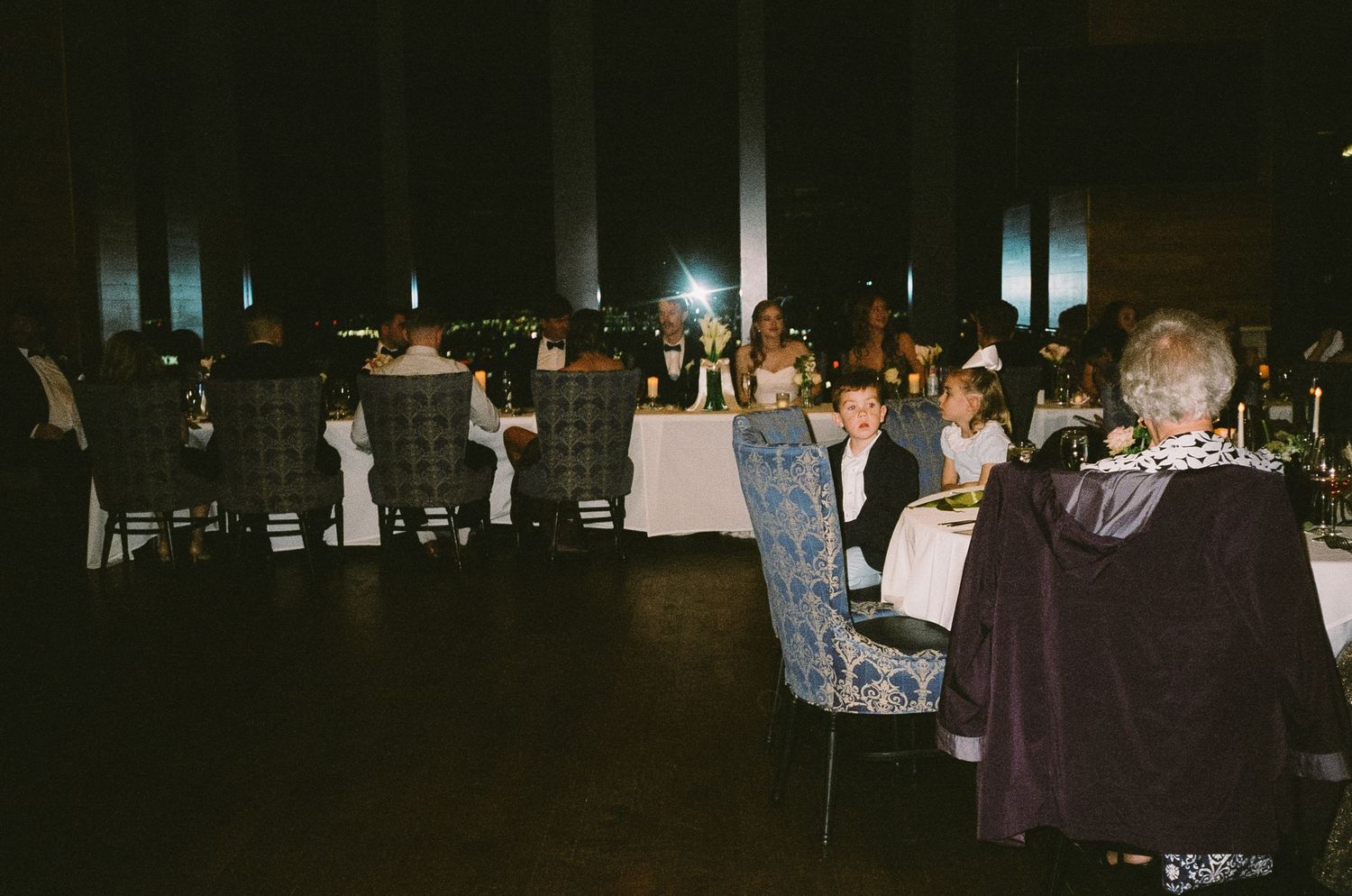 A dimly lit wedding reception with tables and guests visible in the background.