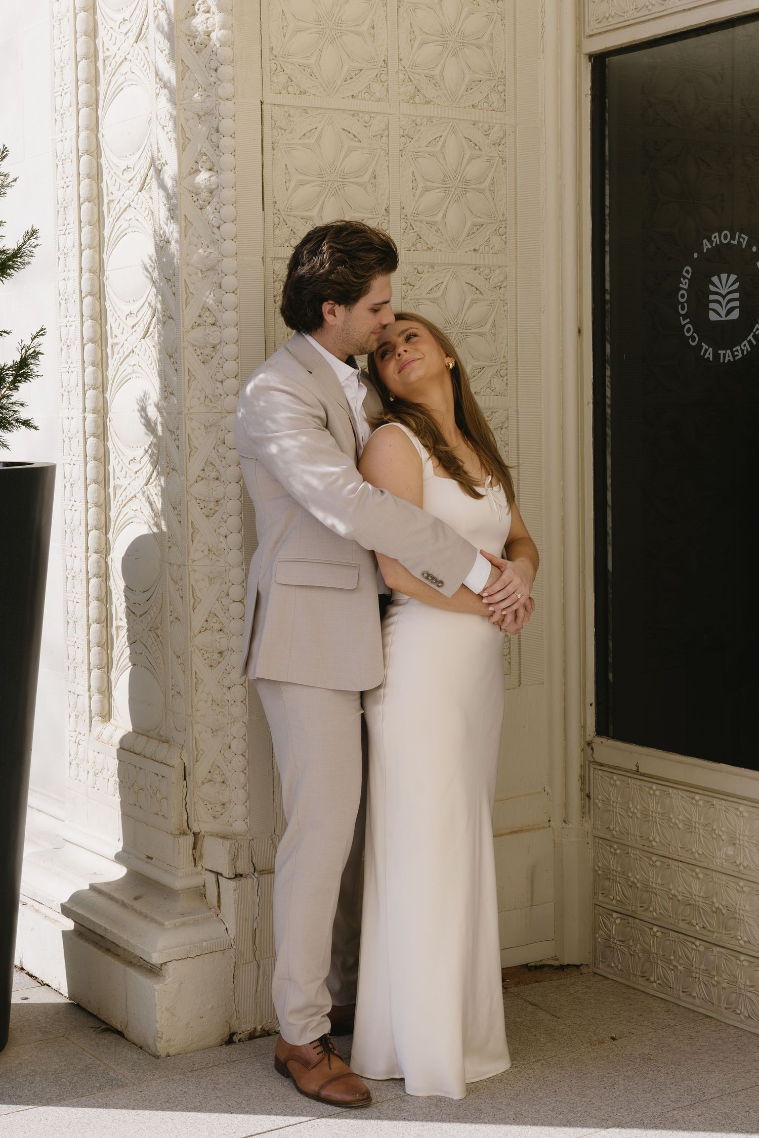 A romantic moment captured between two people in white attire against an ornate wall.