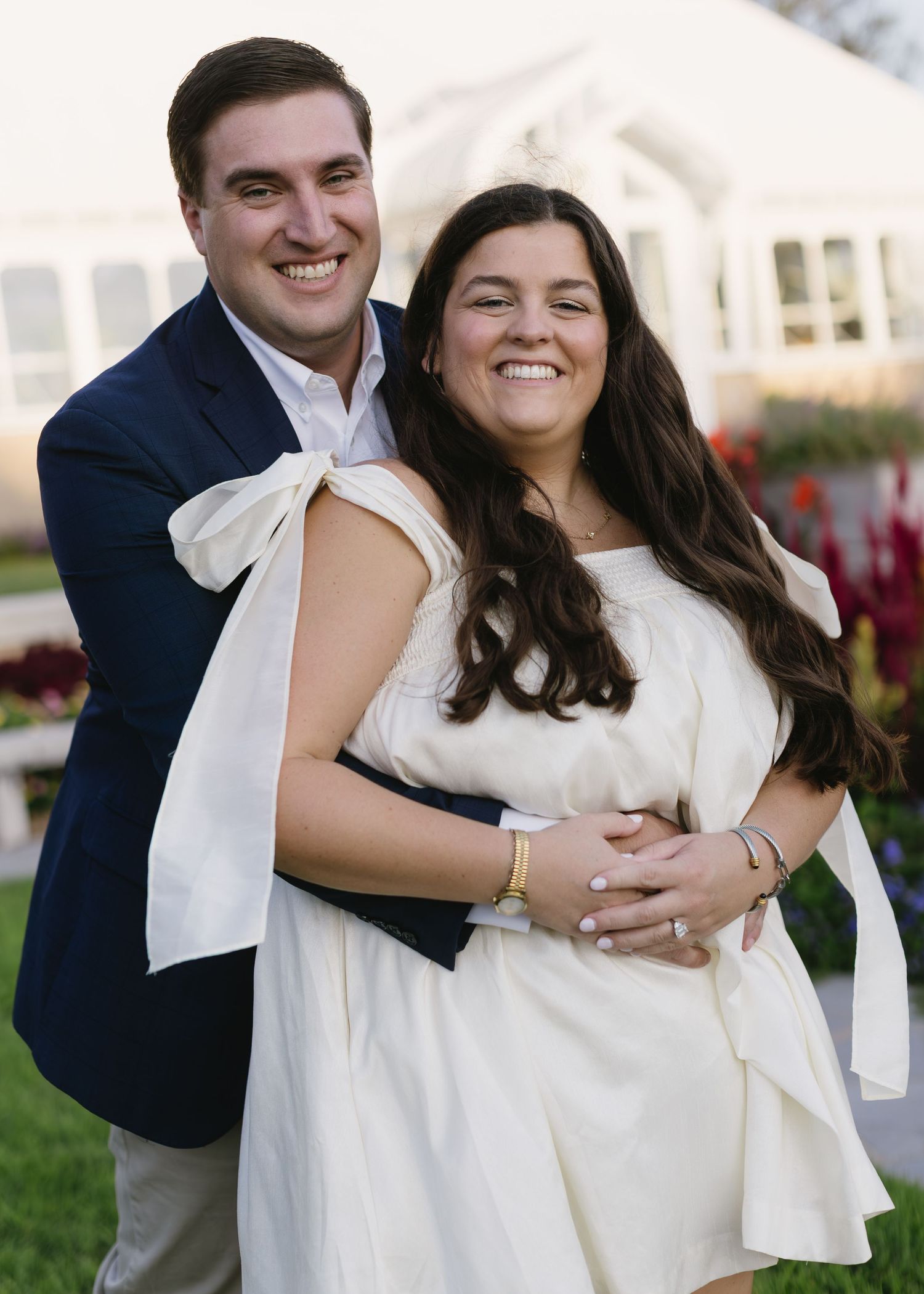 A couple embraces and laughs together in formal wear against a garden backdrop.
