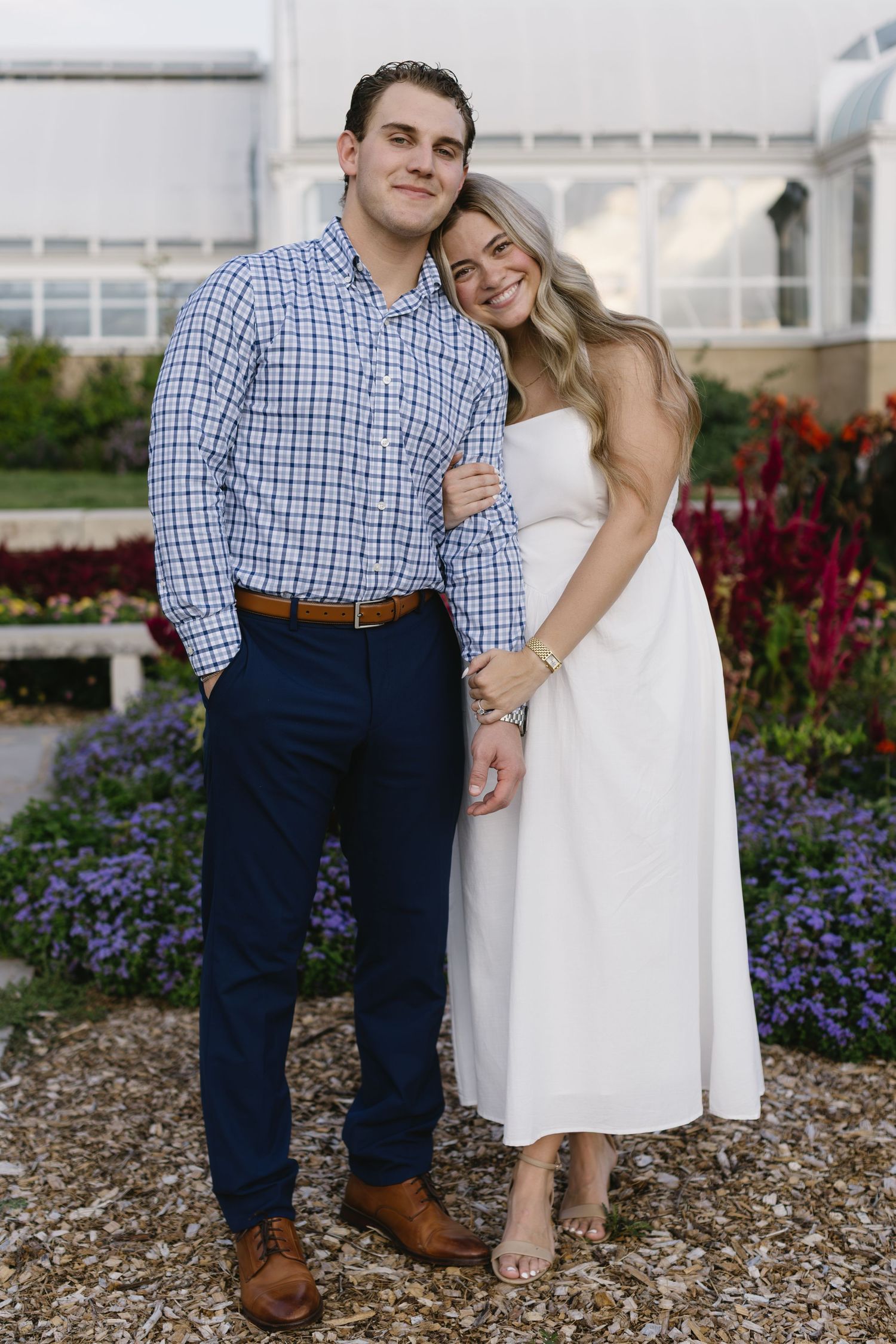 A couple poses together in a garden with blooming flowers, wearing coordinated blue and white outfits.