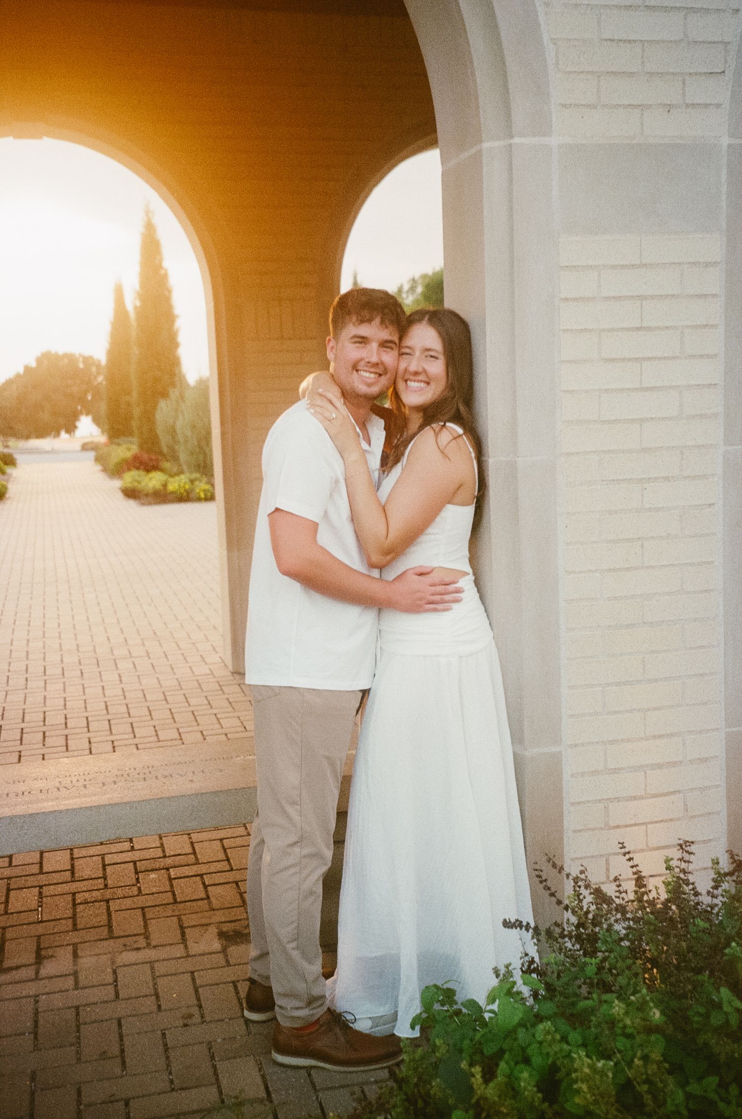 A romantic wedding photo series taken under white arches at sunset with a brick paver patio and garden greenery.