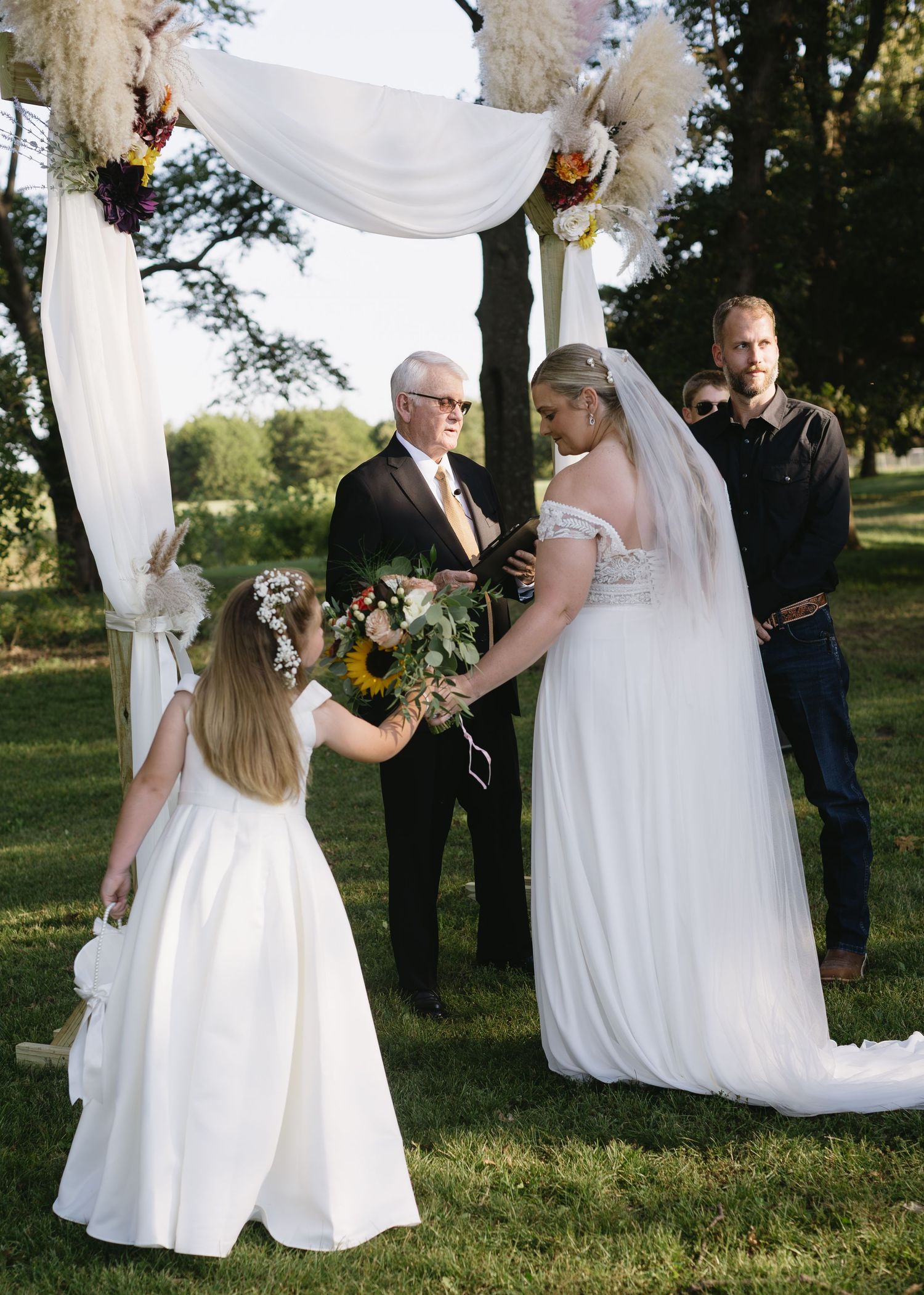 Wedding ceremony setup outdoors with white fabric draped between trees in a garden setting.