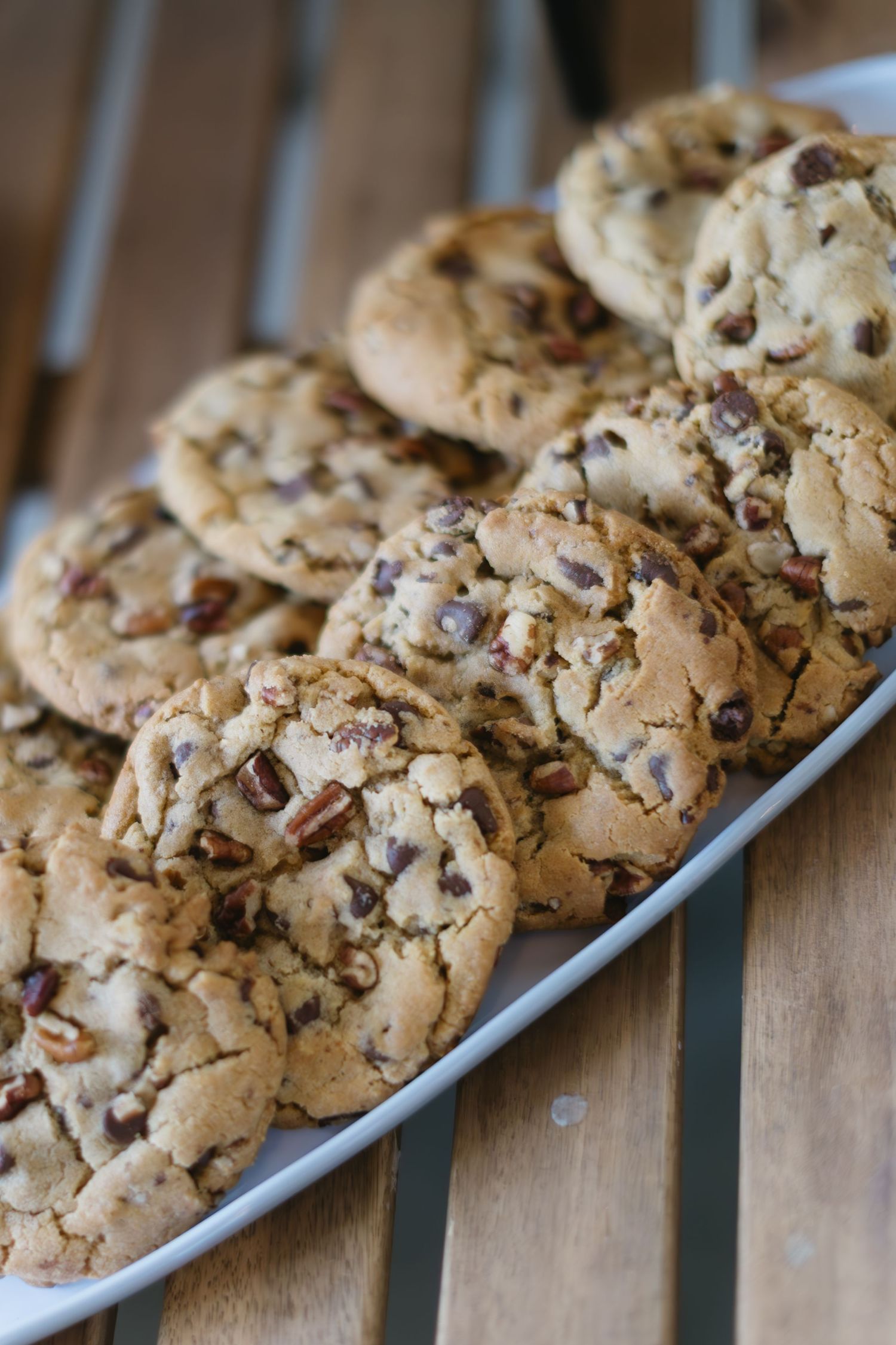 Fresh baked chocolate chip cookies with nuts arranged on a wooden surface.