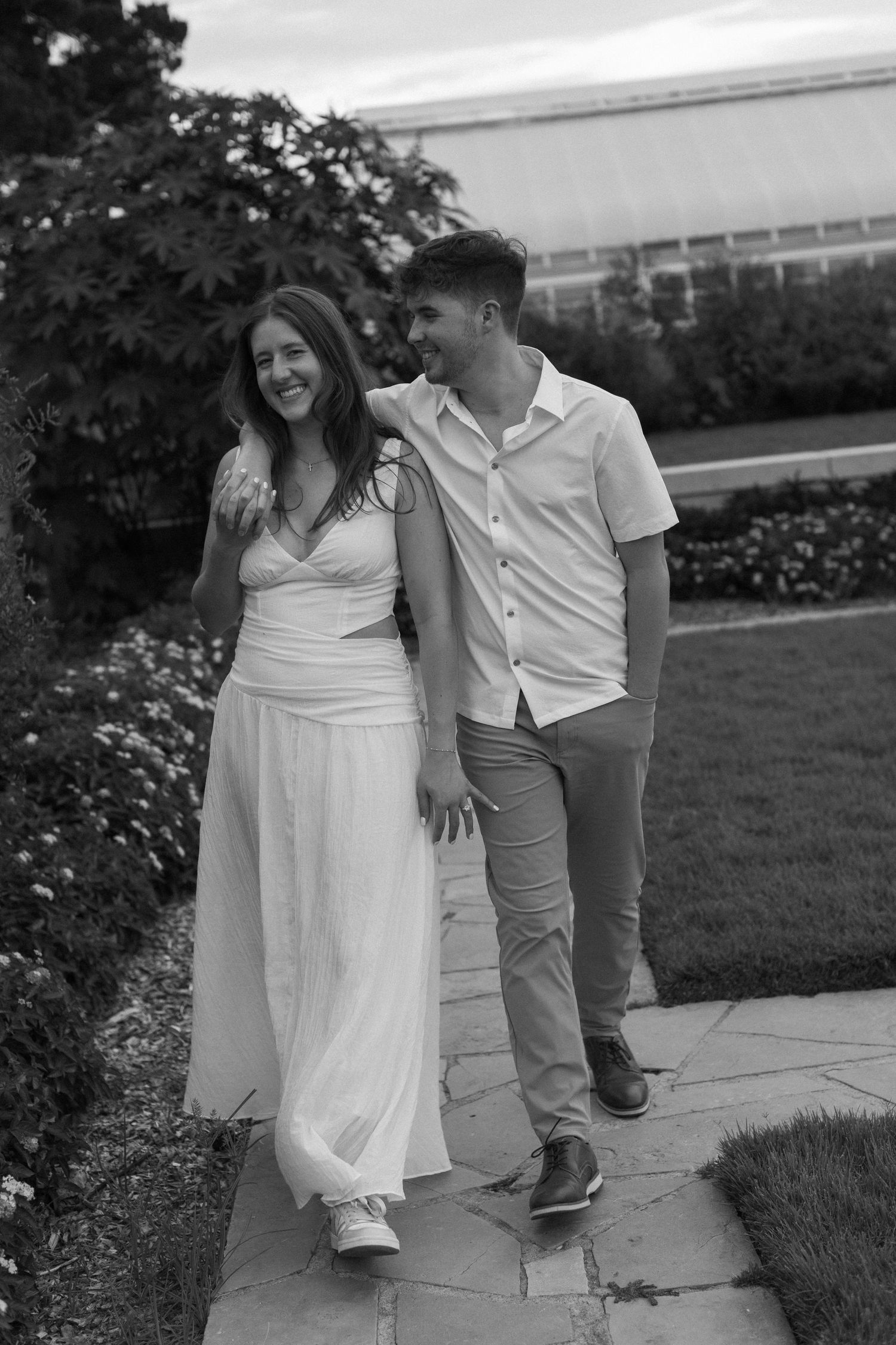 A candid black and white photo of a couple walking and laughing together along a garden path.