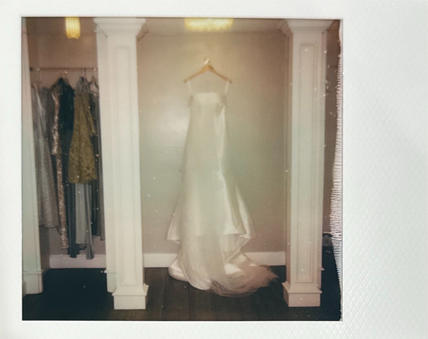 An elegant white wedding gown with train hangs in an alcove beside colorful formal dresses.