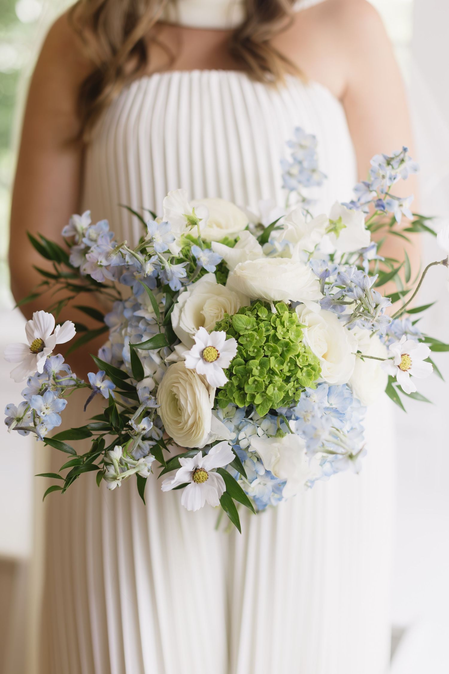 White and blue floral wedding bouquet with roses, hydrangeas and delicate blossoms against a light background.