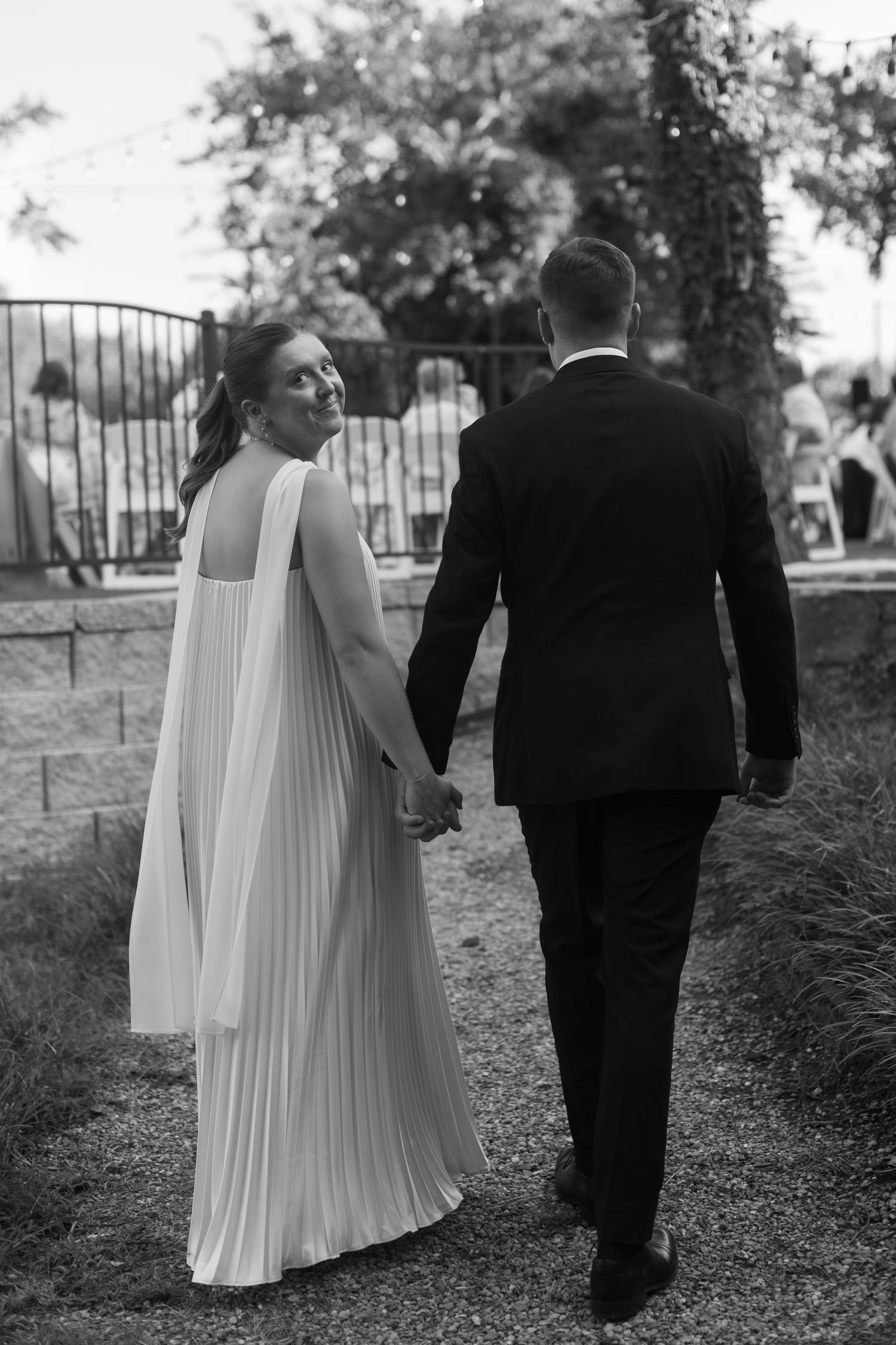 Black and white photograph of couple walking along garden path at wedding.