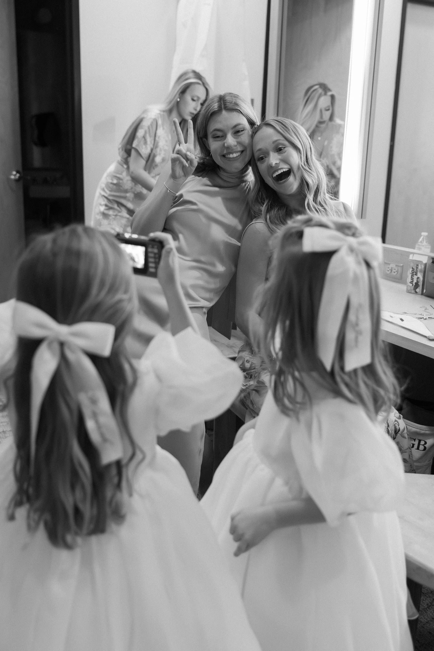 Wedding attendants in white dresses share joyful moments and laughter backstage.