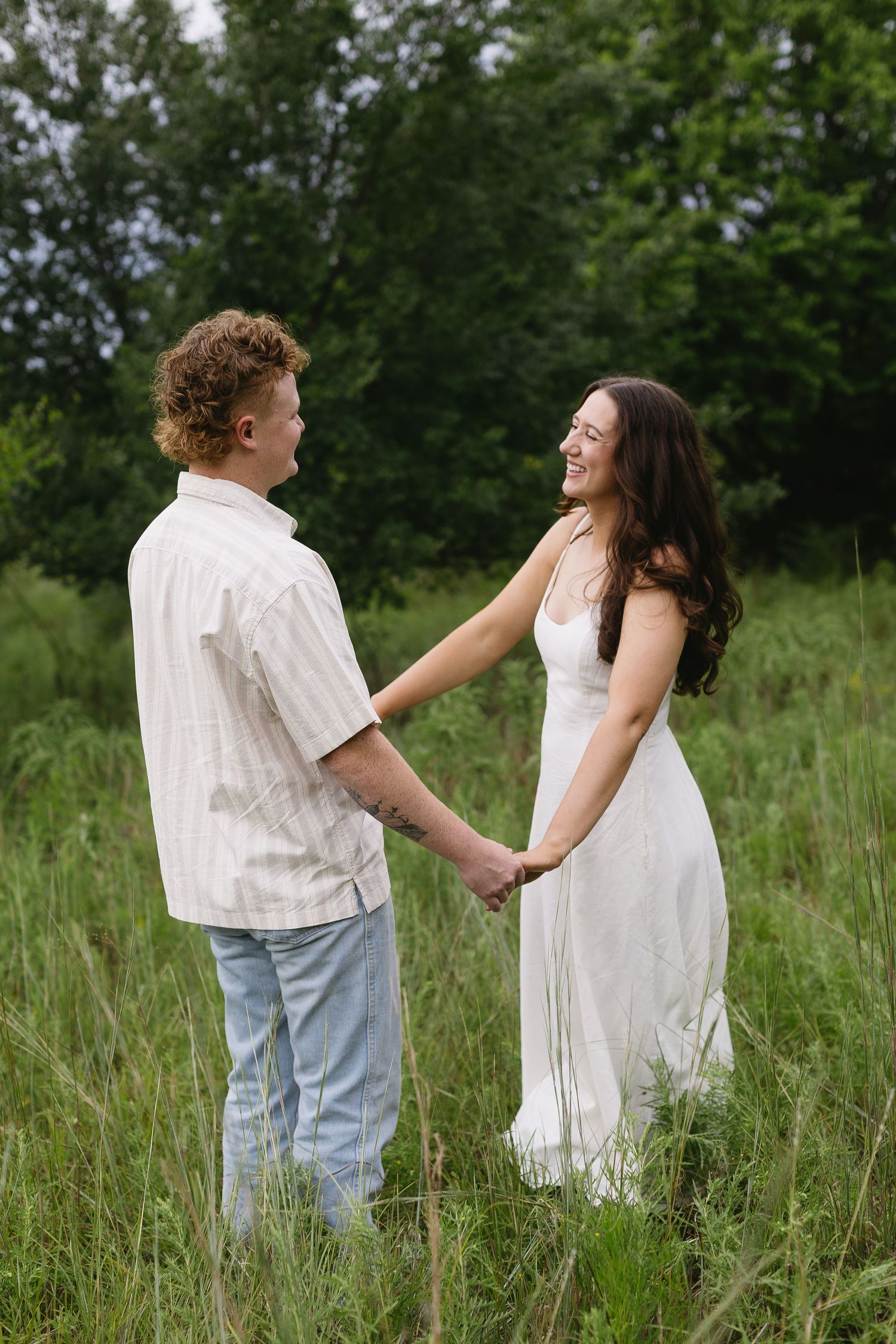 A couple in casual white outfits dancing and laughing together in tall grass.