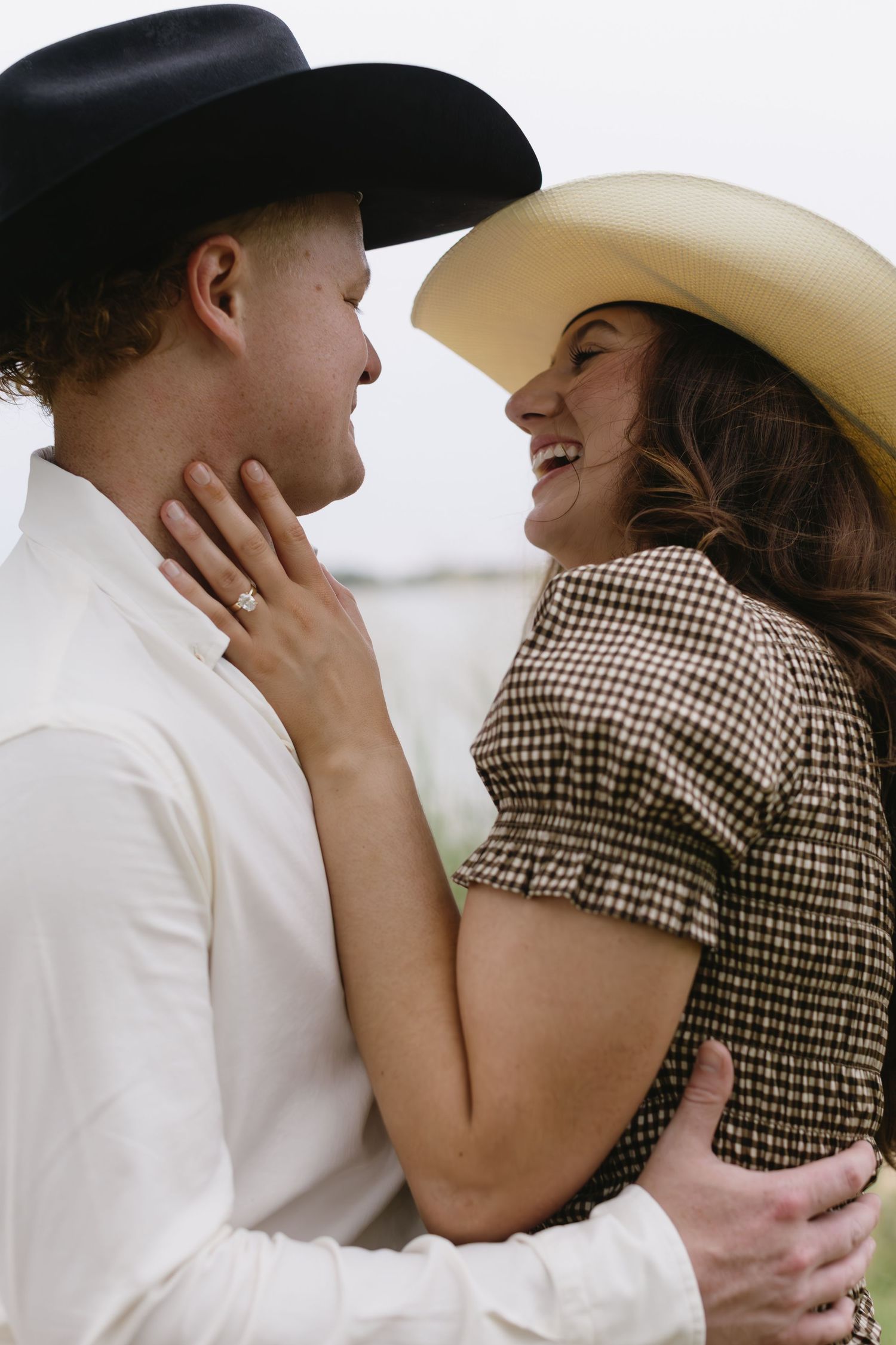 Tender embrace between couple wearing western attire and cowboy hats.
