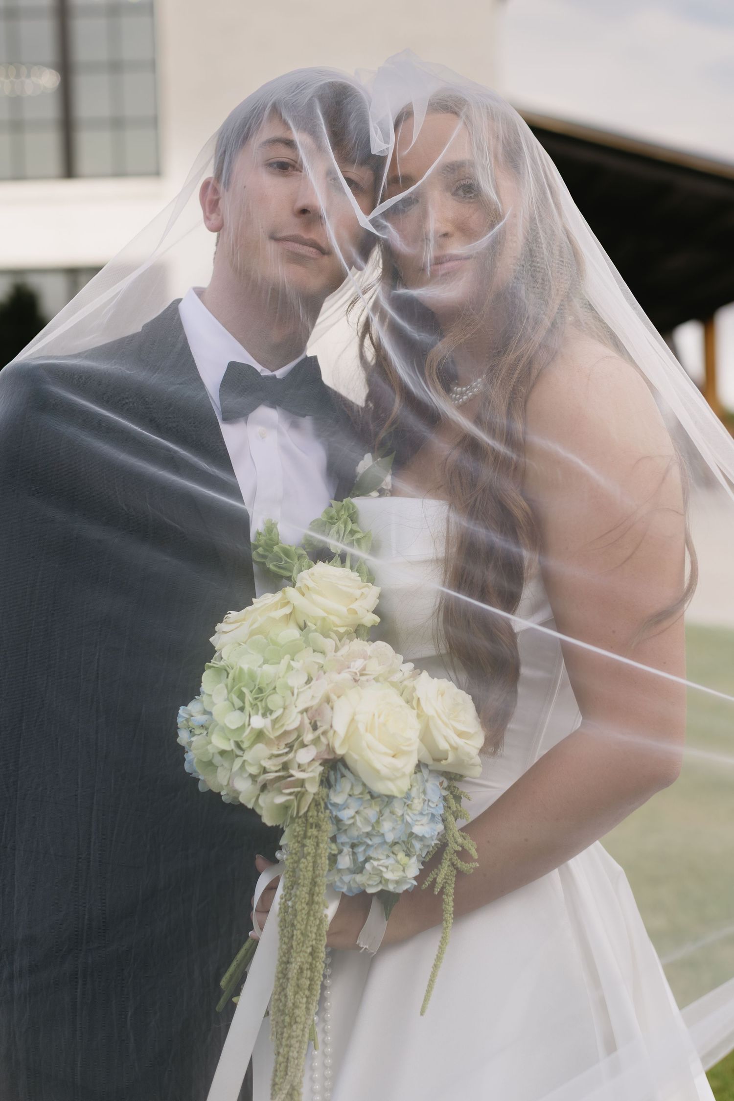 A tender wedding moment captured through a delicate white veil with the bouquet in focus.