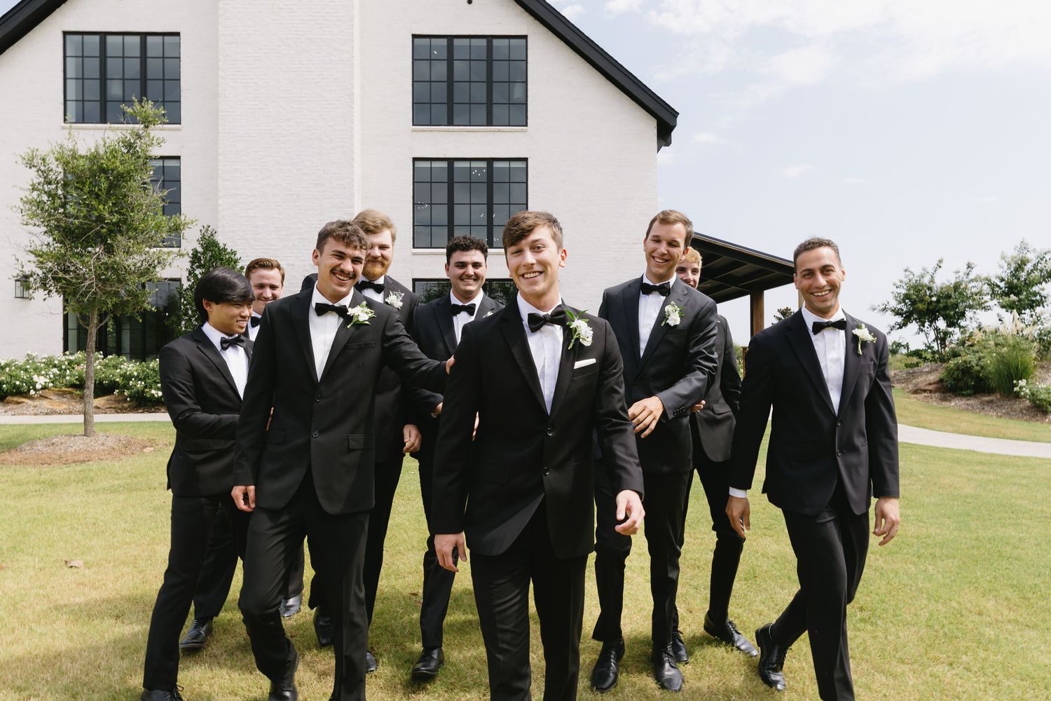 Groomsmen in black tuxedos posing playfully outdoors.