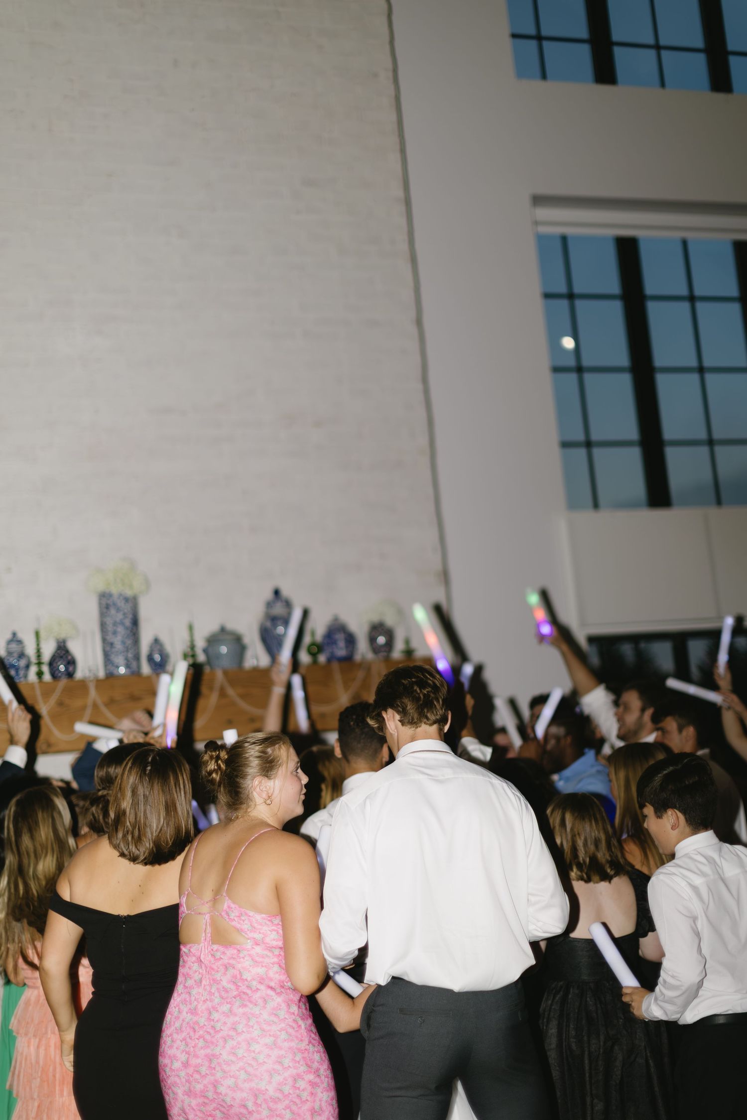 Large crowd of wedding guests dancing and celebrating in a reception hall with white walls.