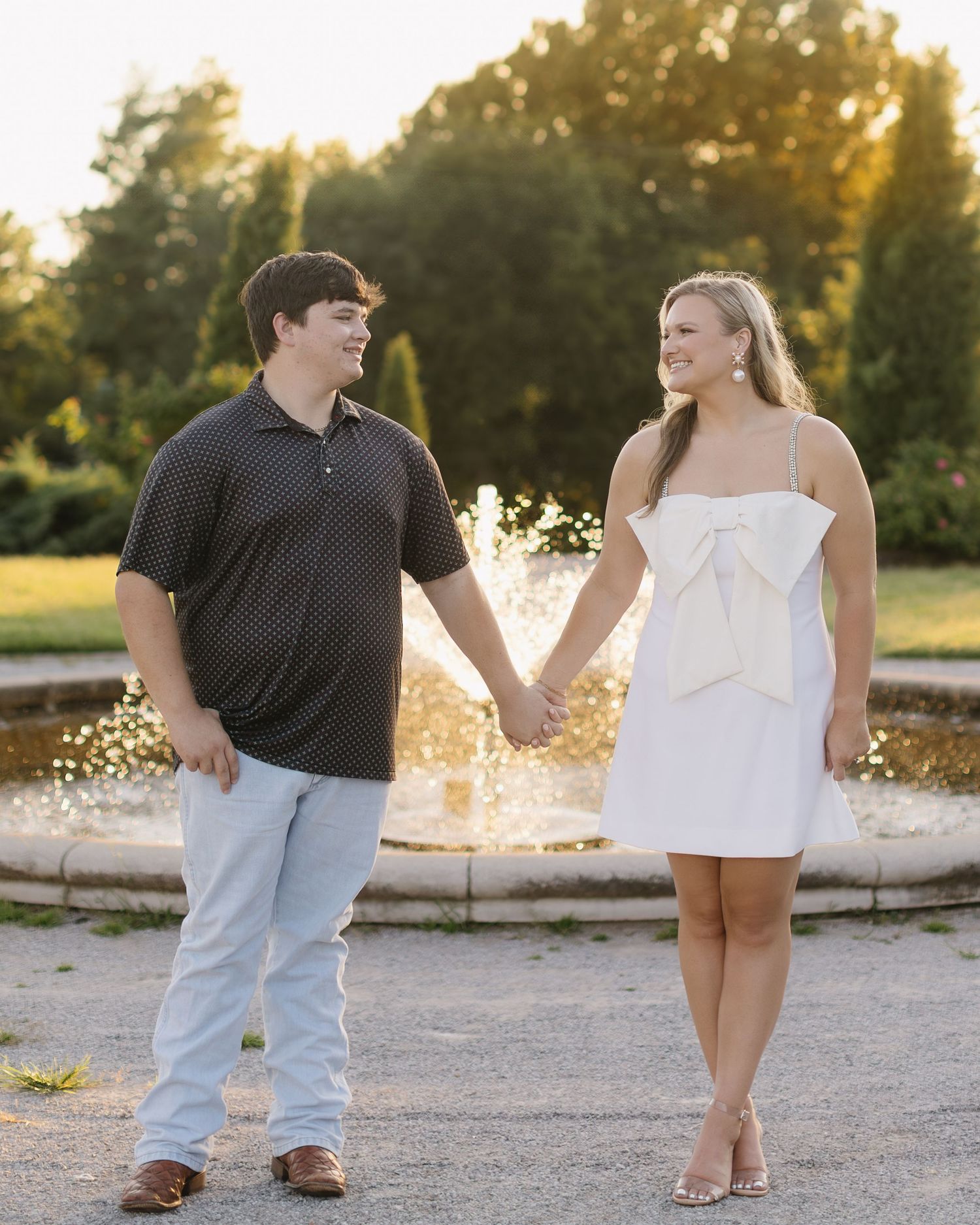 A couple shares a tender moment at sunset on a gravel path with golden sunlight filtering through the trees.
