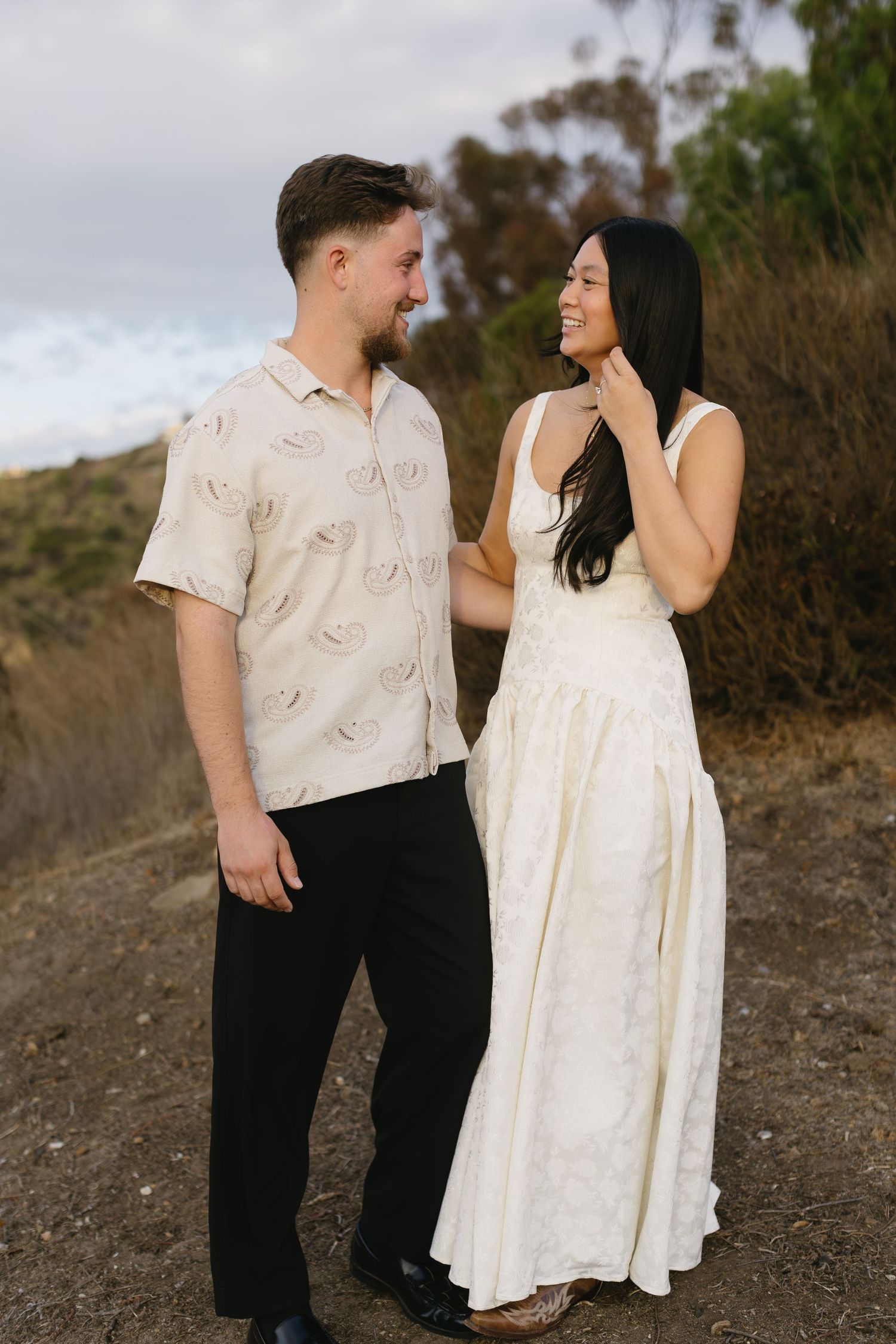 A couple shares playful moments together while posing on a dirt path during an outdoor photo session.