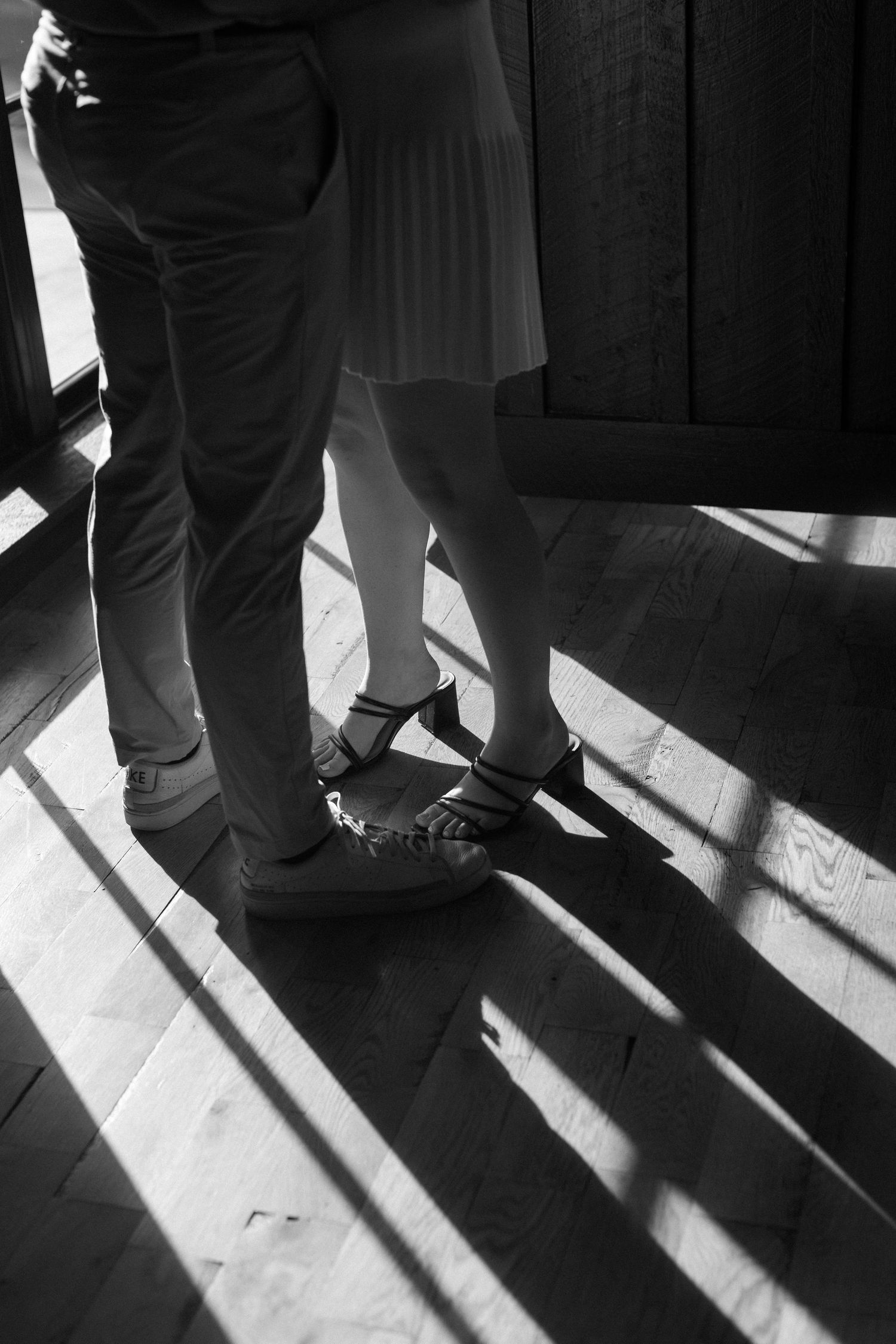 Black and white image of shadows and feet on a sunlit floor.