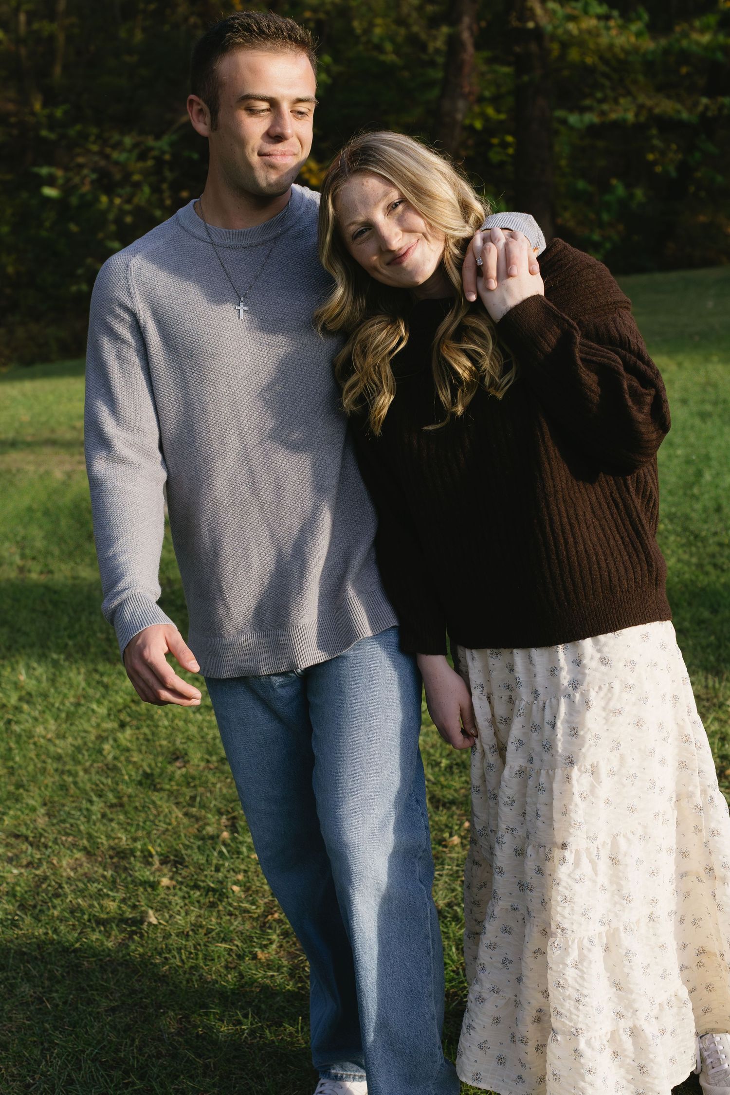 A couple embraces while standing in a sunny outdoor setting.