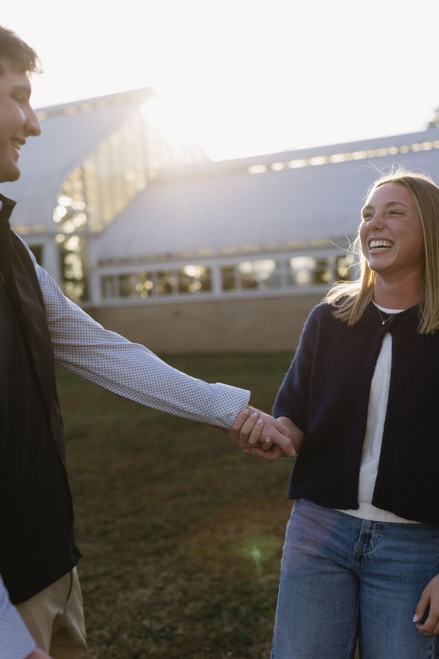 A couple shares a joyful moment together outdoors during golden hour, laughing and holding hands.