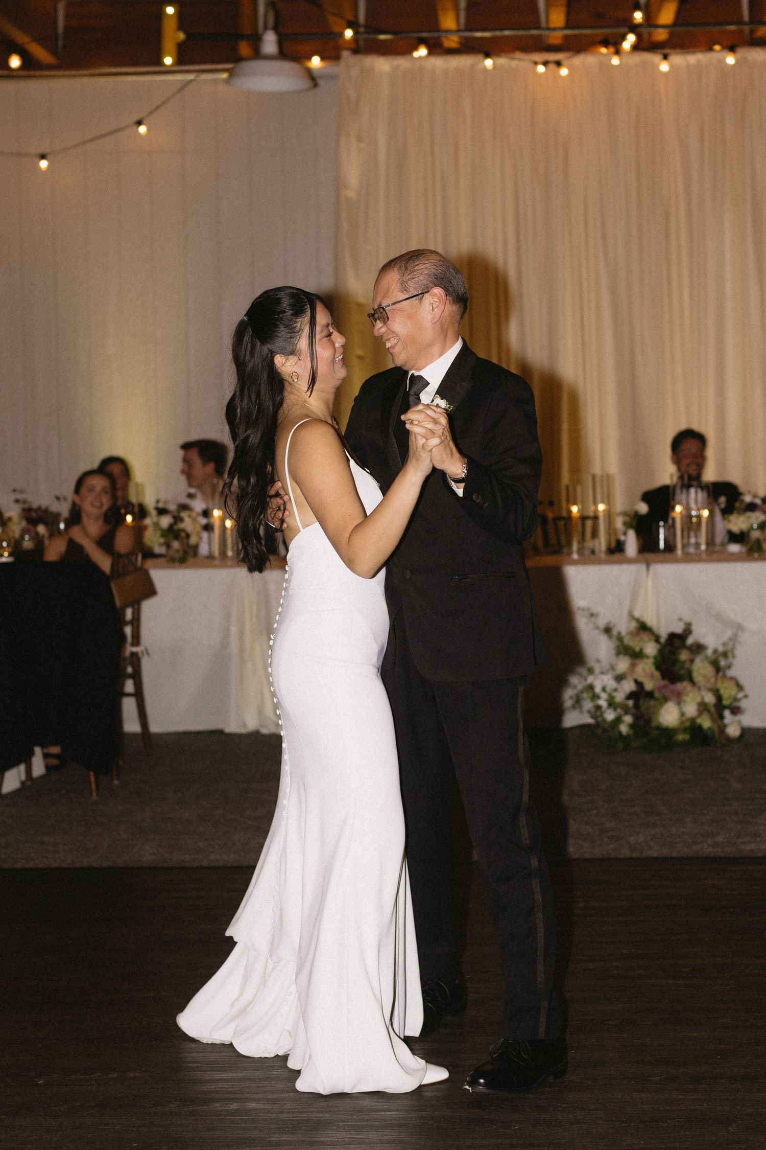 First dance at wedding reception with couple in white dress and black tuxedo.