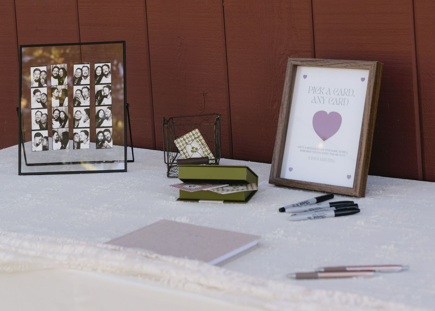Wedding guest book table setup with photo display, pens, and heart-themed decor.