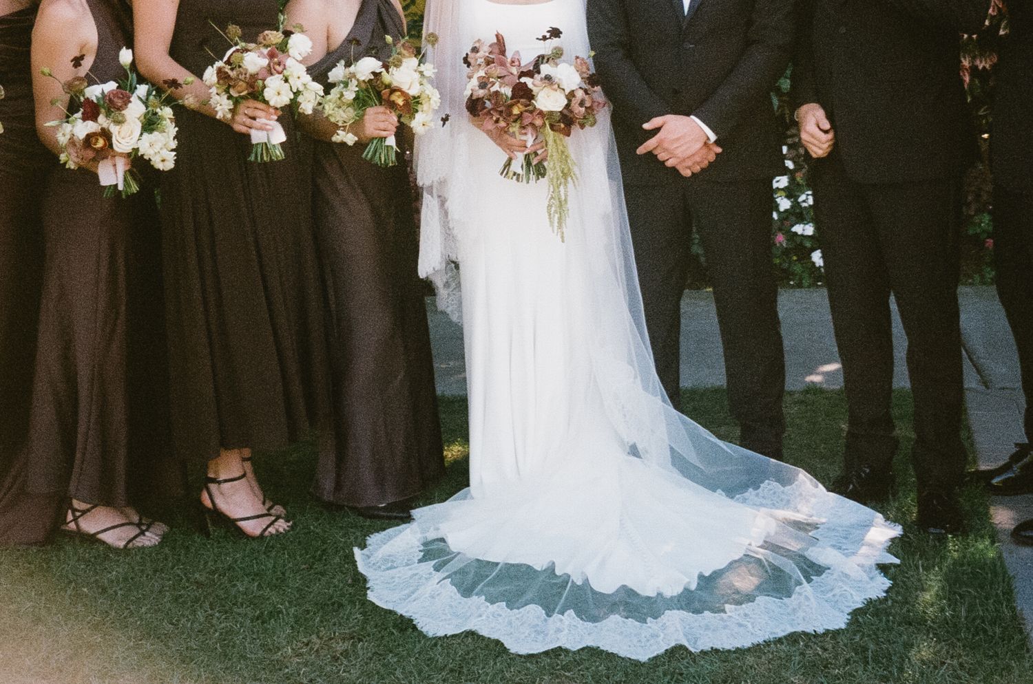 Bottom portion of wedding party attire showing formal dresses and suits.
