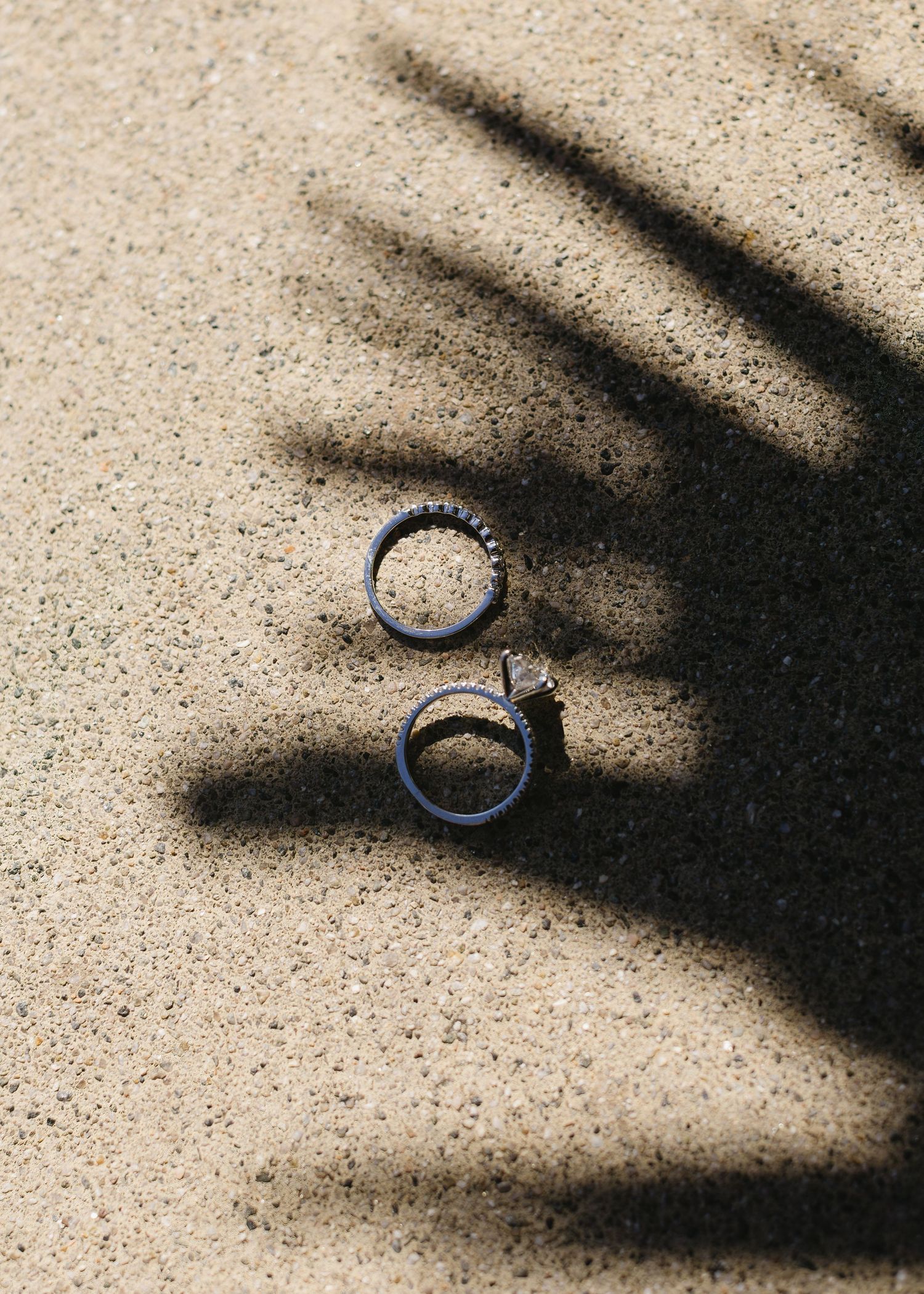Close-up sequence showing a wedding ring being placed on sand with dramatic shadows.
